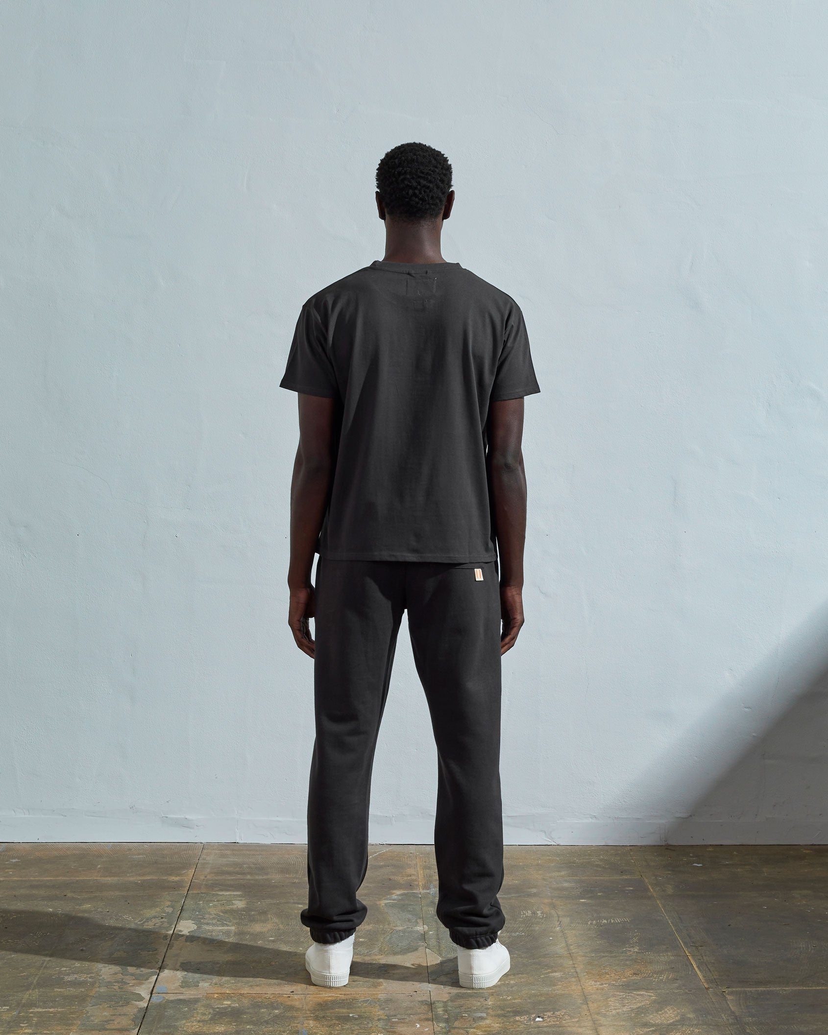 Full-length back view of model wearing faded black, relaxed cut organic cotton #7006 jersey T-shirt by Uskees paired with matching pants.