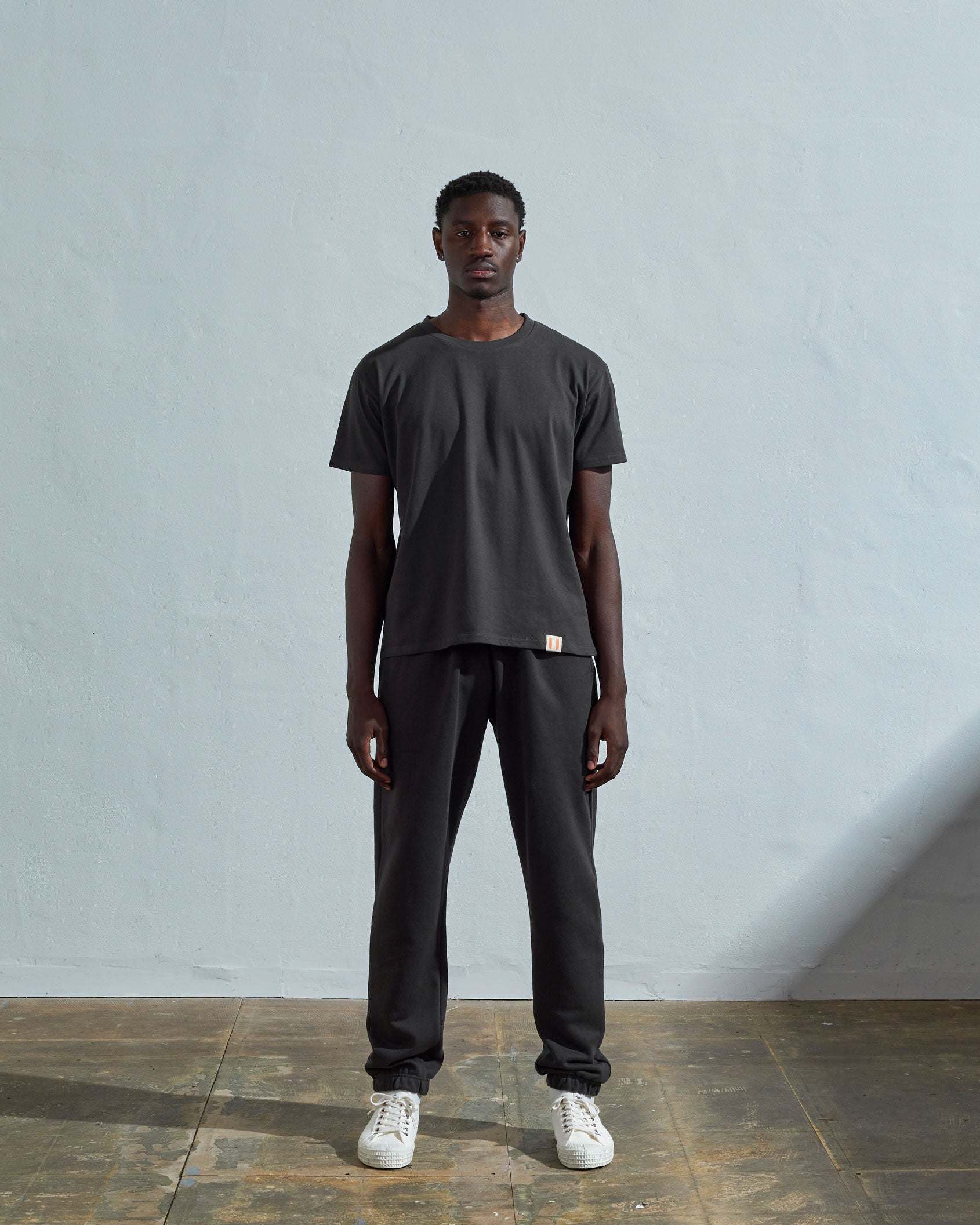 Full-length front view of model wearing faded black organic cotton #7006 jersey T-shirt by Uskees paired with matching pants.