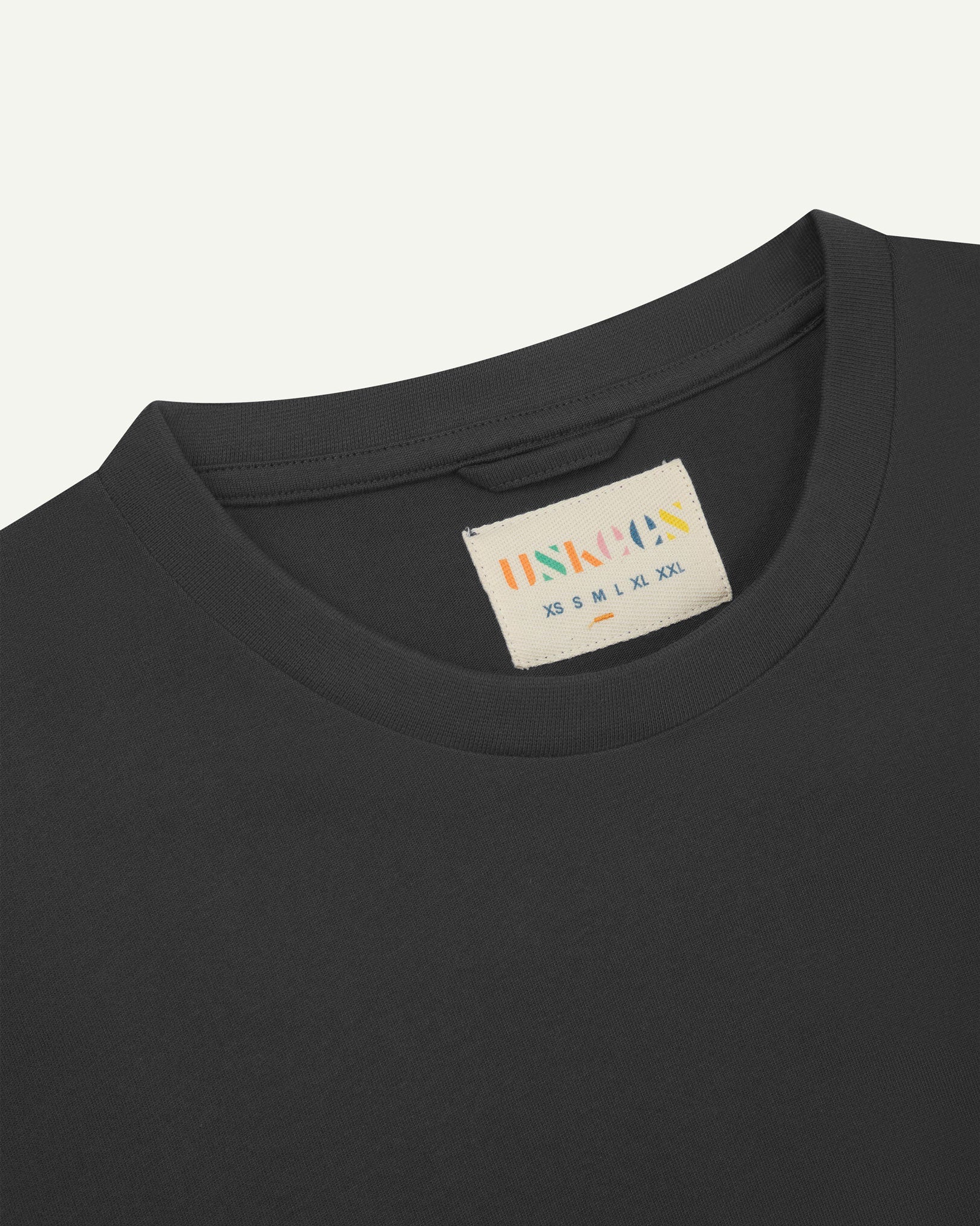 Neckline close-up of Uskees faded black organic cotton T-shirt showing hanging loop and branding label.