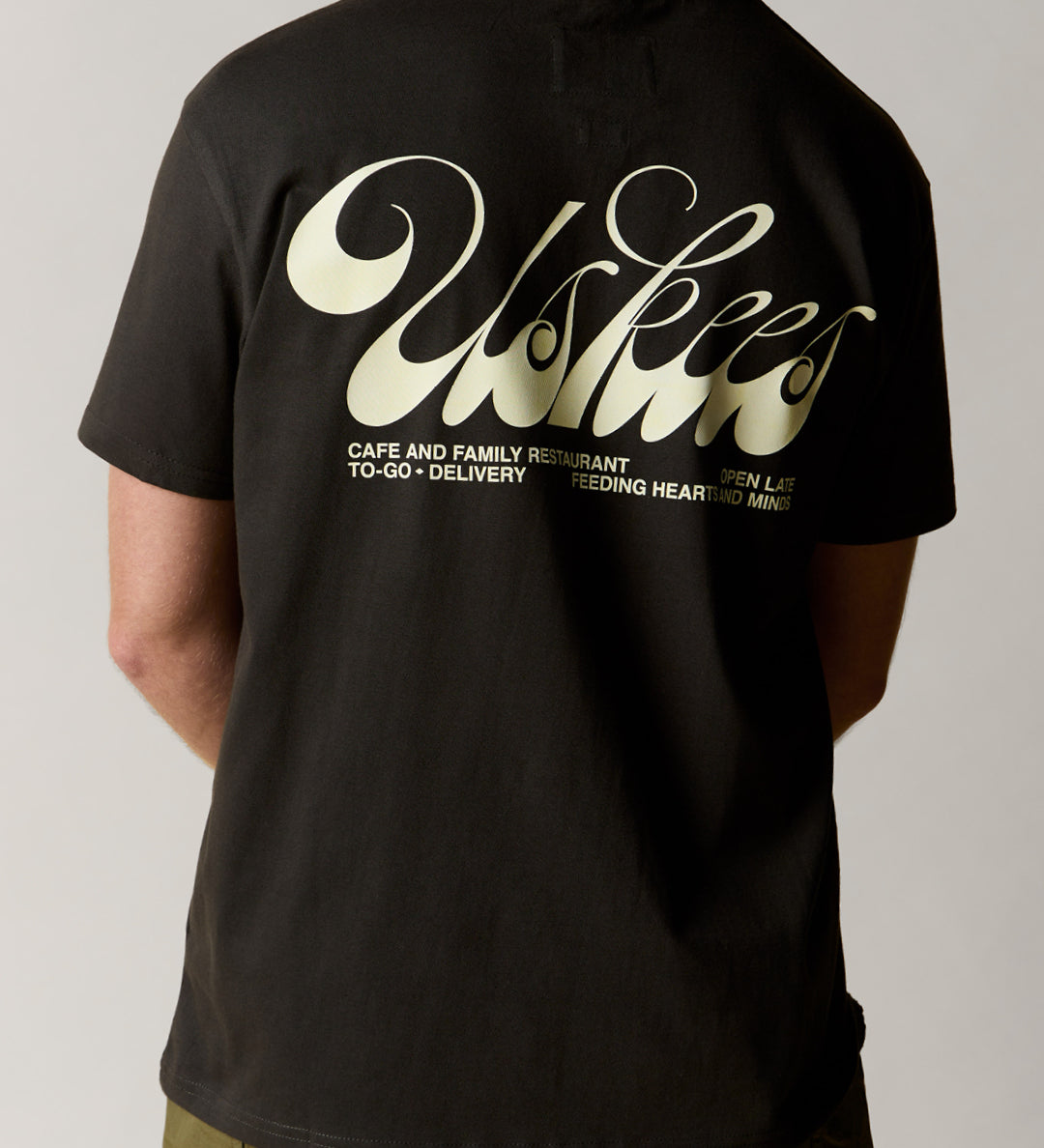 Reverse view of man wearing the uskees faded black men's 'diner' tee, demonstrating the comfortable fit and the large, white 'diner' logo displayed across the back.