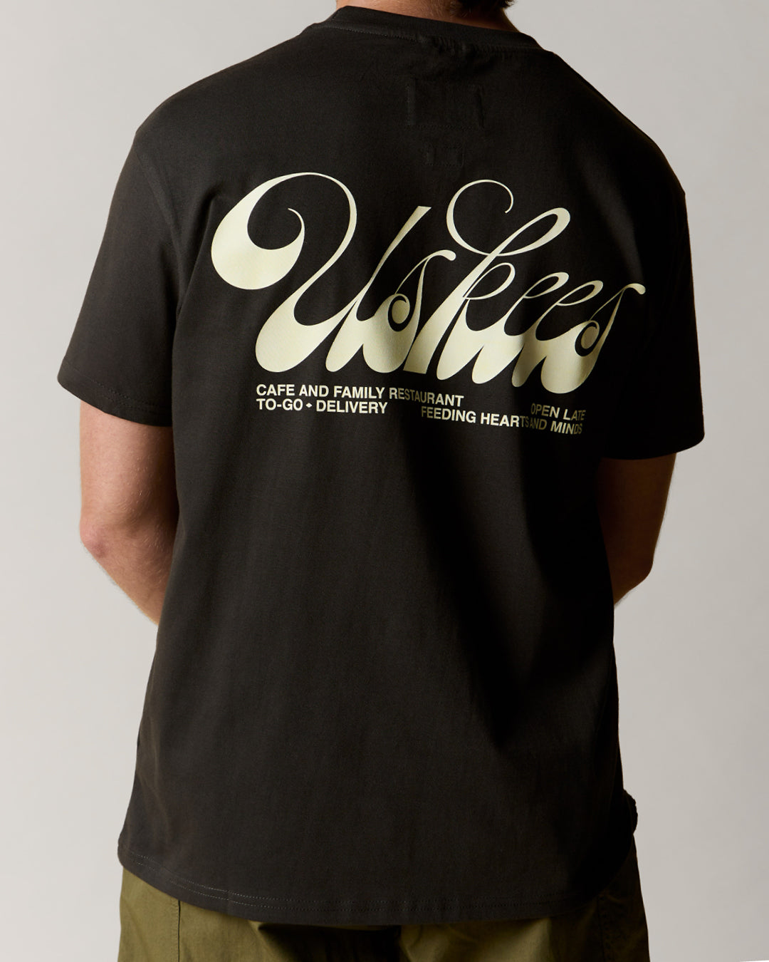 Reverse view of man wearing the uskees faded black men's 'diner' tee, demonstrating the comfortable fit and the large, white 'diner' logo displayed across the back.