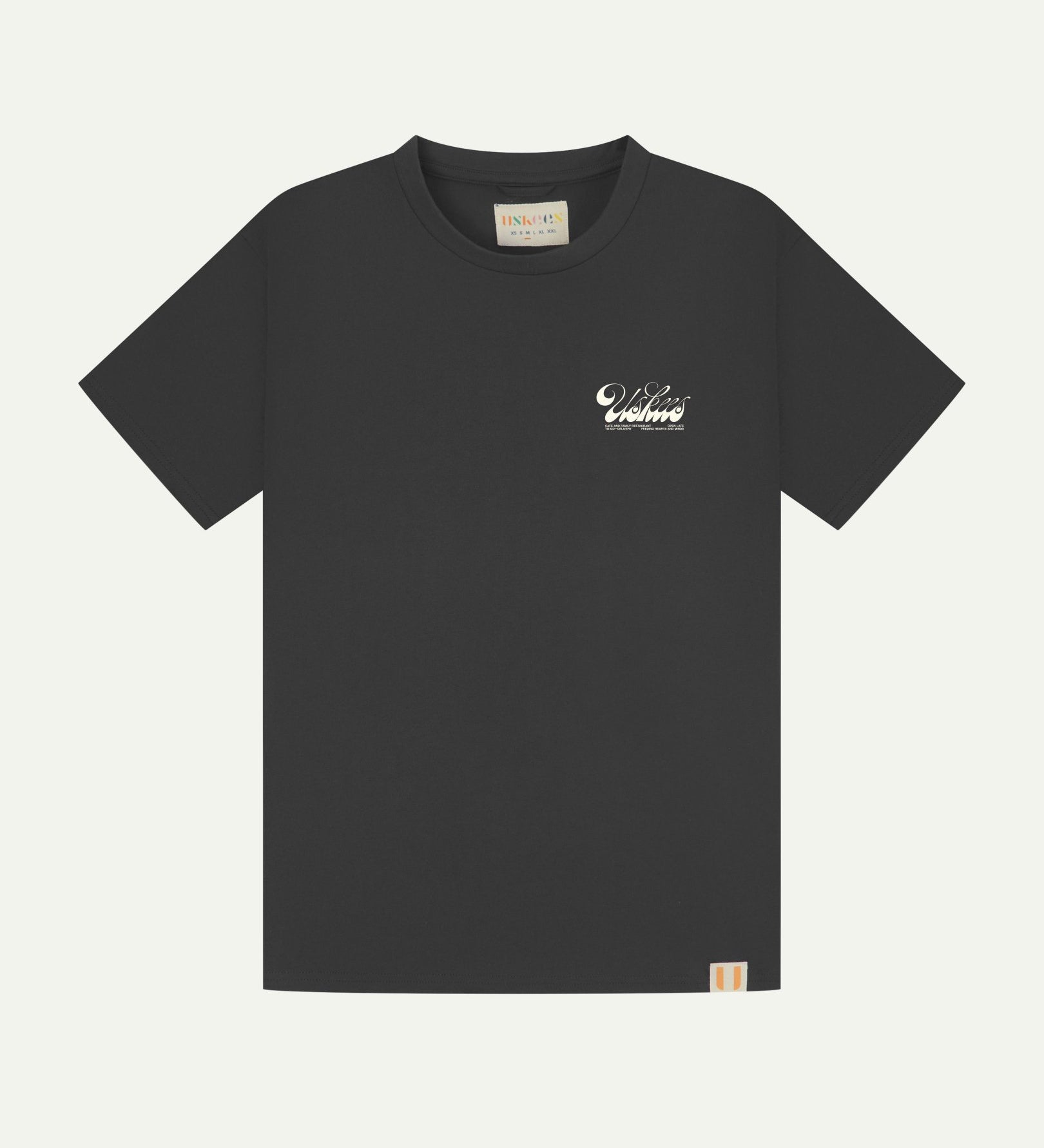 Full flat view of faded black organic cotton Uskees T-shirt for men, showing the small white 'diner' logo on the breast and the Uskees branding labels on the neck and hem.