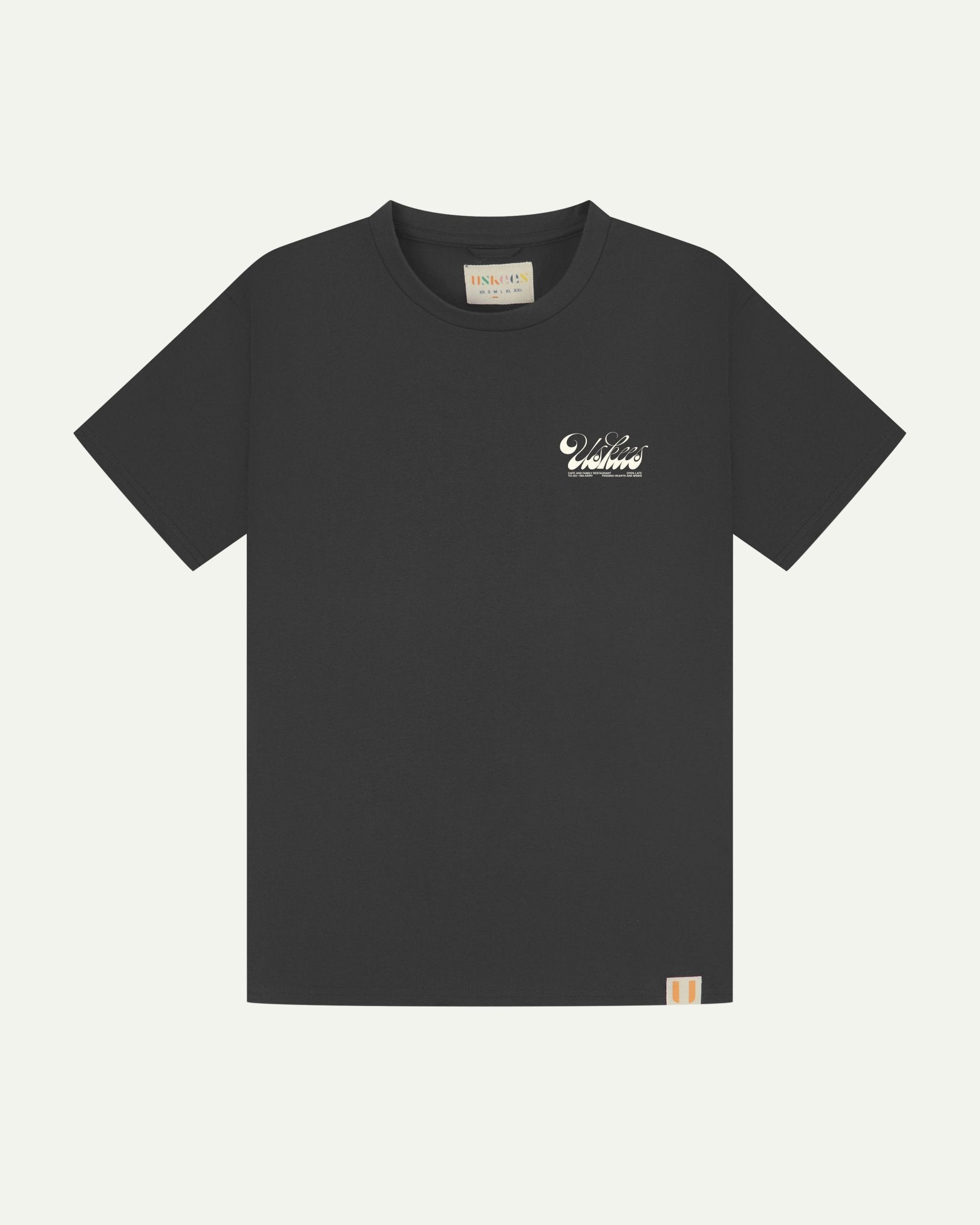 Full flat view of faded black organic cotton Uskees T-shirt for men, showing the small white 'diner' logo on the breast and the Uskees branding labels on the neck and hem.