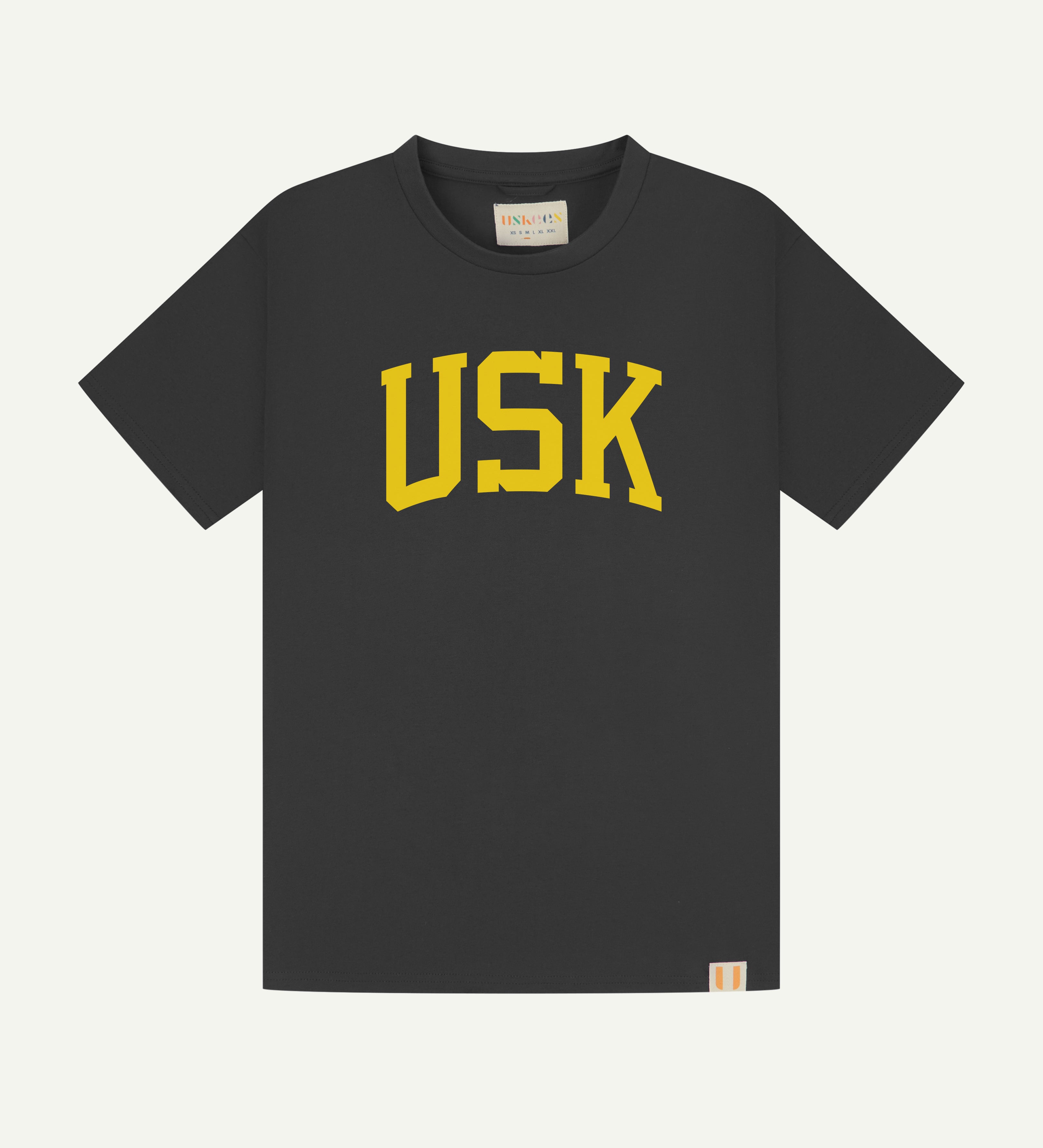 Full flat view of faded black organic cotton signature T-shirt for men, showing the varsity inspired 'USK' logo in yellow on the chest, and the Uskees branding labels on the neck and hem.