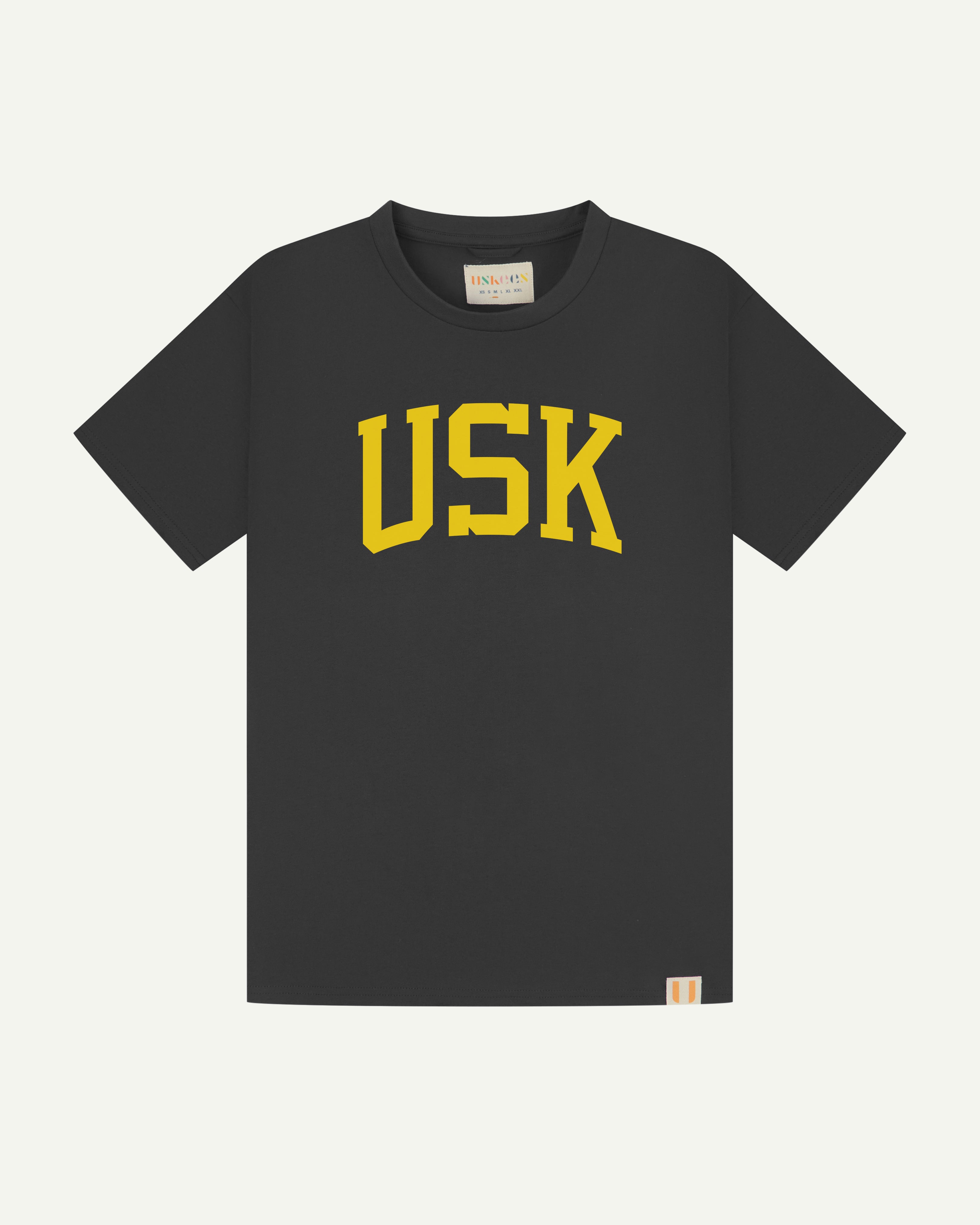 Full flat view of faded black organic cotton signature T-shirt for men, showing the varsity inspired 'USK' logo in yellow on the chest, and the Uskees branding labels on the neck and hem.