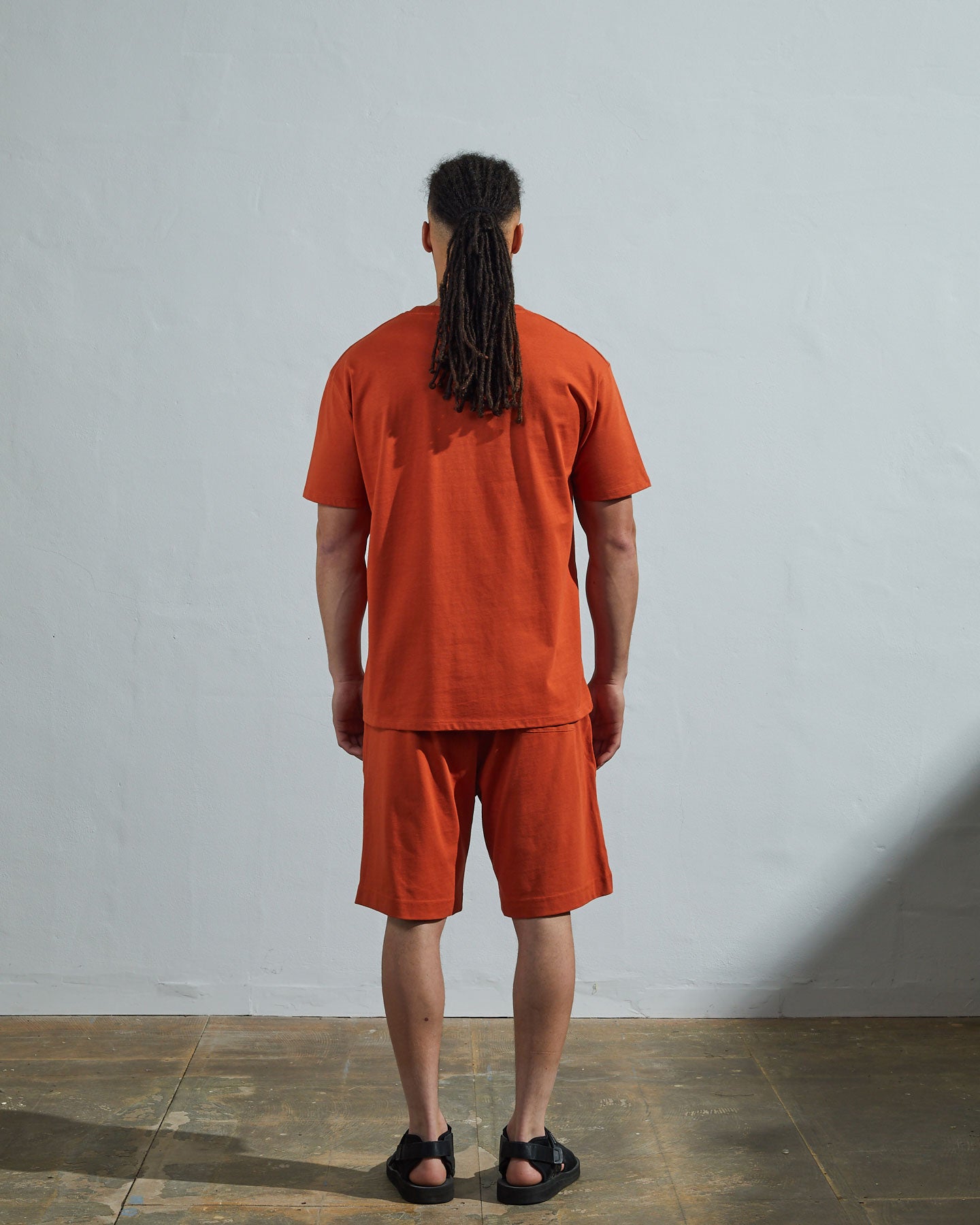 Full-length back view of model wearing golden-orange, relaxed cut organic cotton #7006 jersey T-shirt by Uskees paired with matching #7007 shorts.