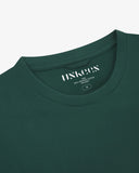 Neckline close-up of Uskees green organic cotton T-shirt showing hanging loop and branding stamp.