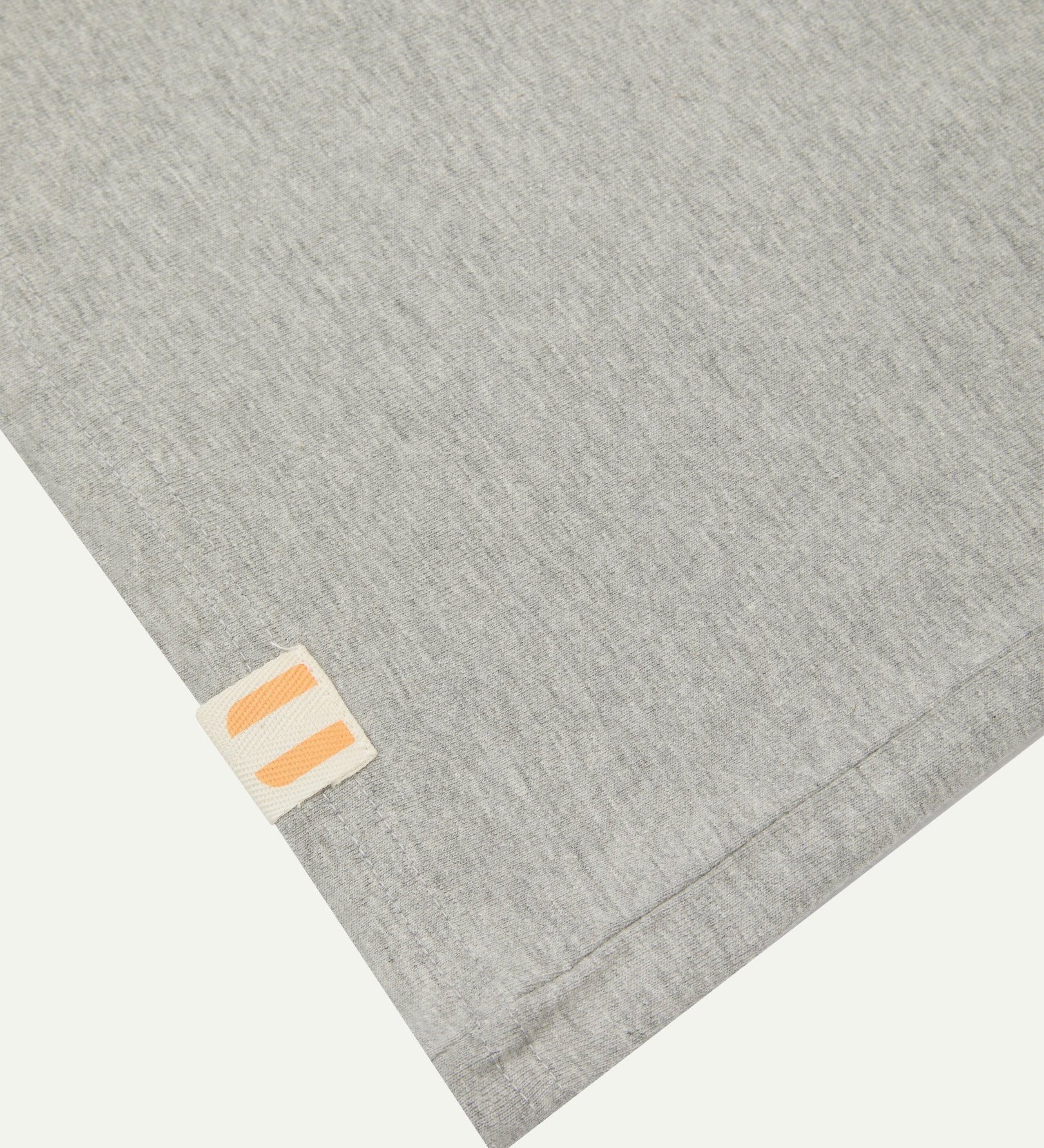 Hem close-up of the grey marl organic cotton T-shirt showing texture of the medium weight organic cotton jersey and the small square Uskees branding tag.