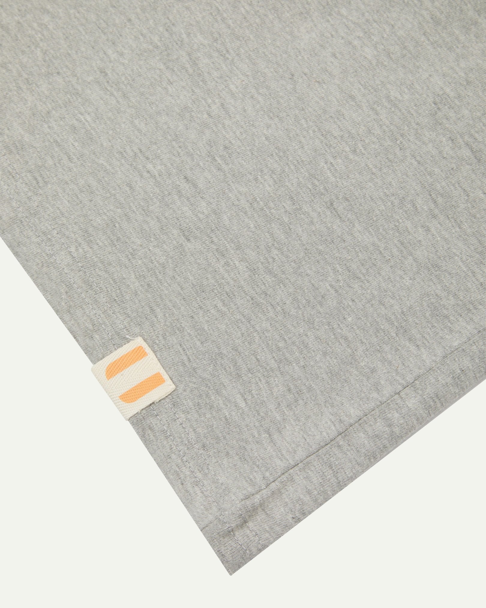 Hem close-up of the grey marl organic cotton T-shirt showing texture of the medium weight organic cotton jersey and the small square Uskees branding tag.