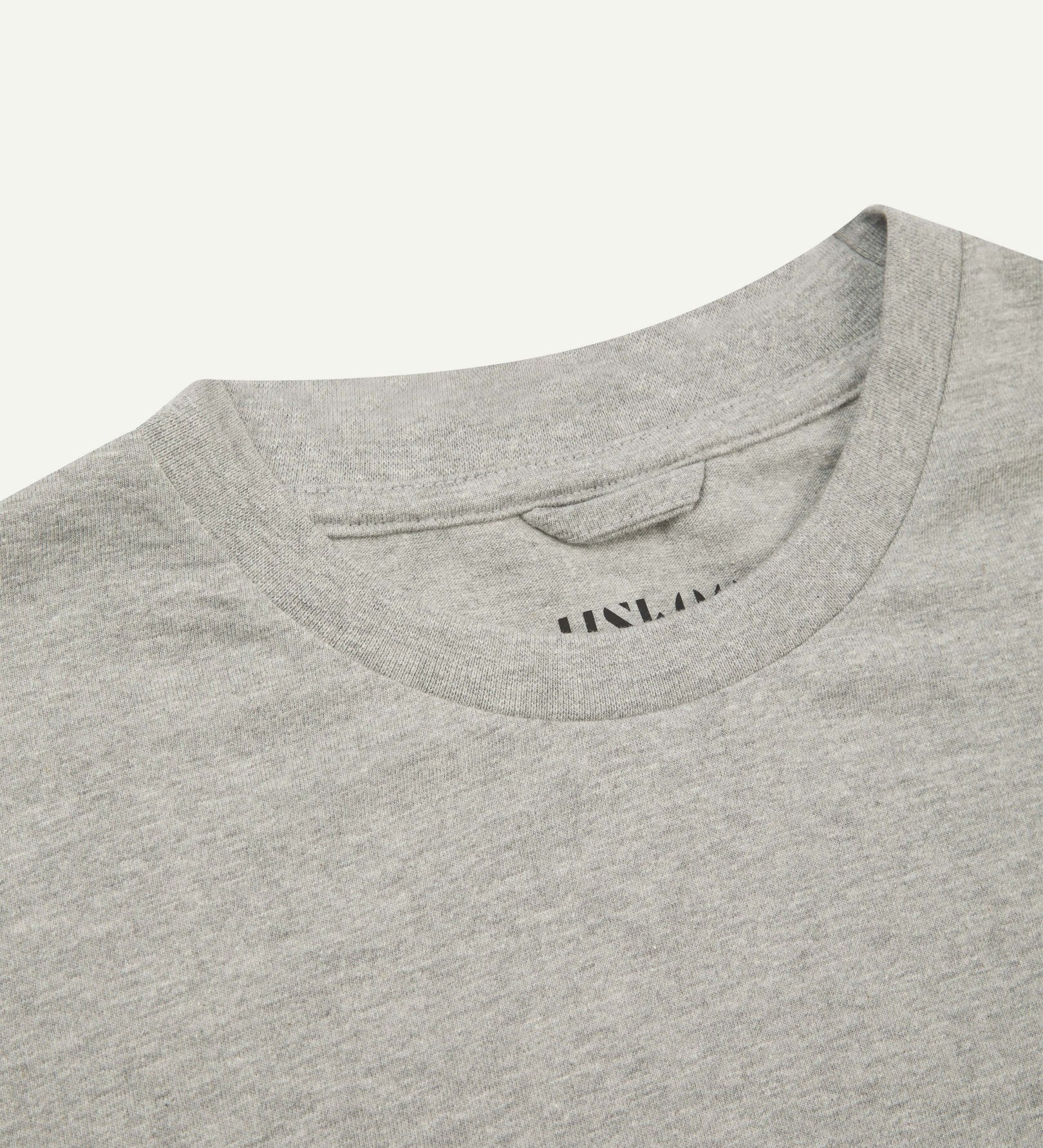 Neckline close-up of Uskees grey marl organic cotton T-shirt showing hanging loop and branding stamp.