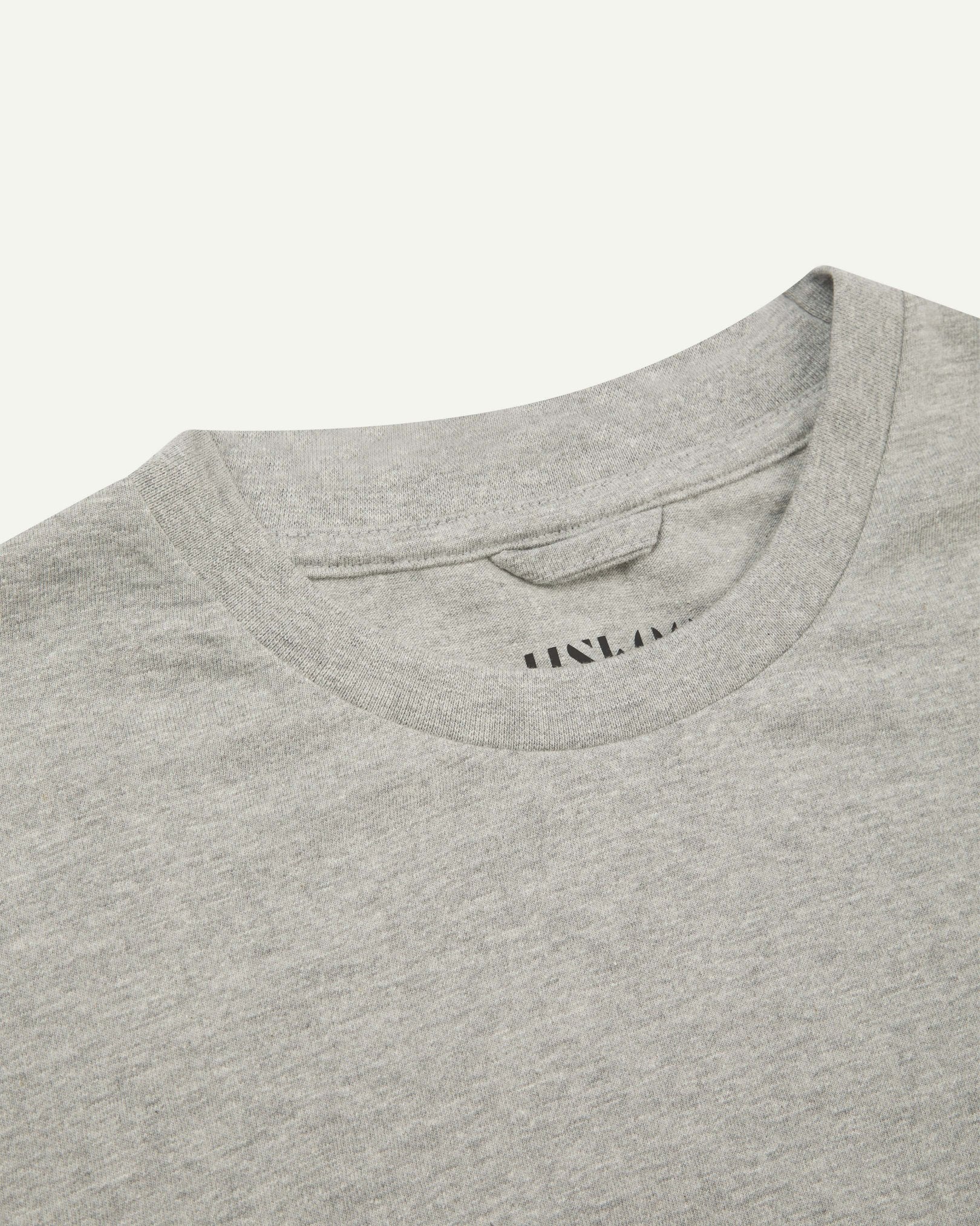 Neckline close-up of Uskees grey marl organic cotton T-shirt showing hanging loop and branding stamp.