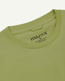 Neckline close-up of Uskees green-yellow organic cotton T-shirt showing hanging loop and branding stamp.