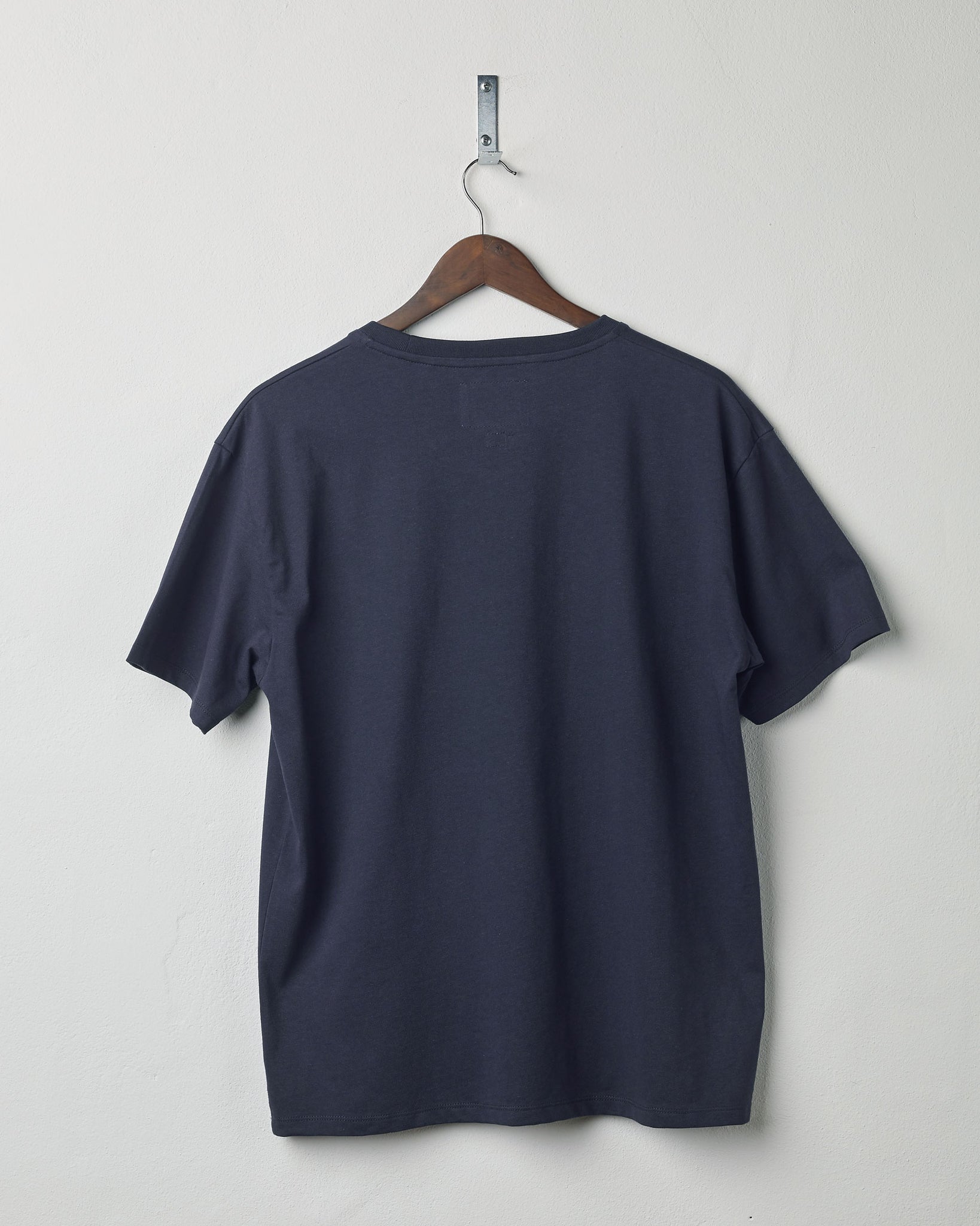 Back view of midnight blue organic cotton #7006 jersey T-shirt by Uskees. Presented on hanger against white background.