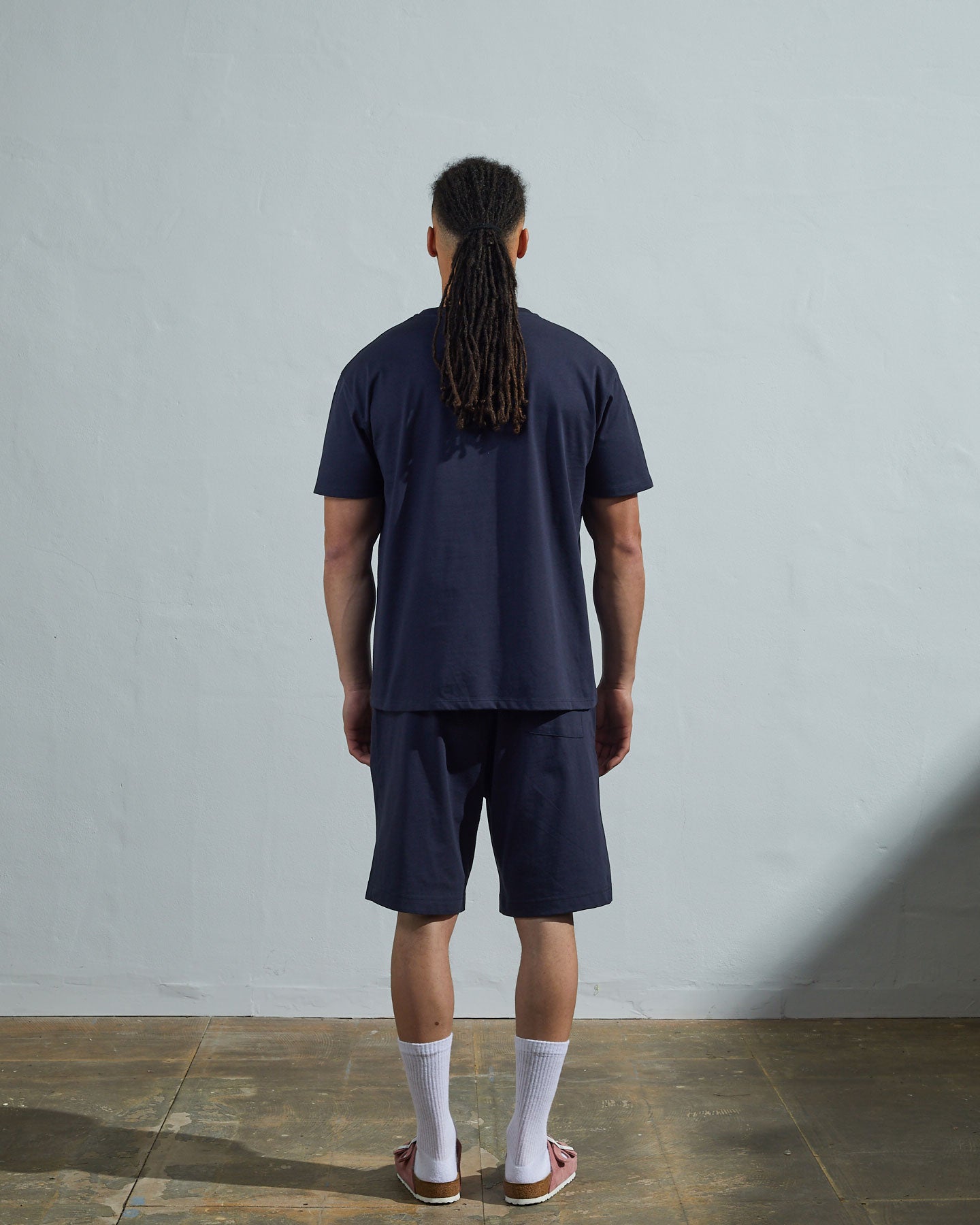 Full-length back view of model wearing midnight blue, relaxed cut organic cotton #7006 jersey T-shirt by Uskees paired with matching #7007 shorts.