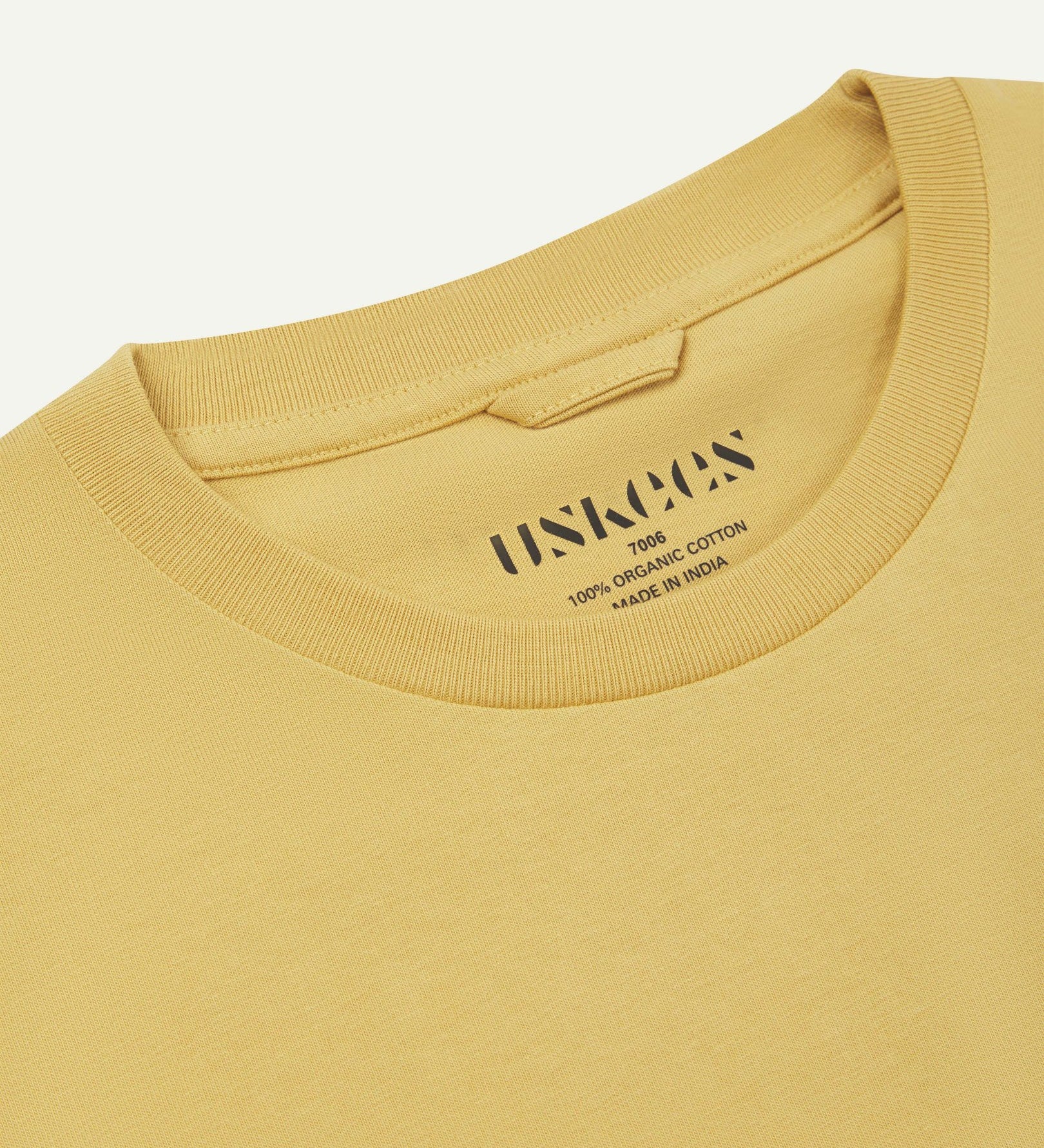 Neckline close-up of Uskees sandstone organic cotton T-shirt showing hanging loop and branding stamp.