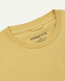 Neckline close-up of Uskees sandstone organic cotton T-shirt showing hanging loop and branding stamp.