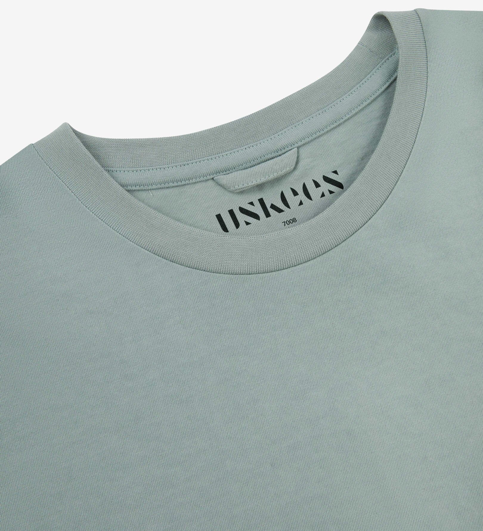 Neckline close-up of Uskees green-grey 'steel' coloured organic cotton T-shirt showing hanging loop and branding stamp.