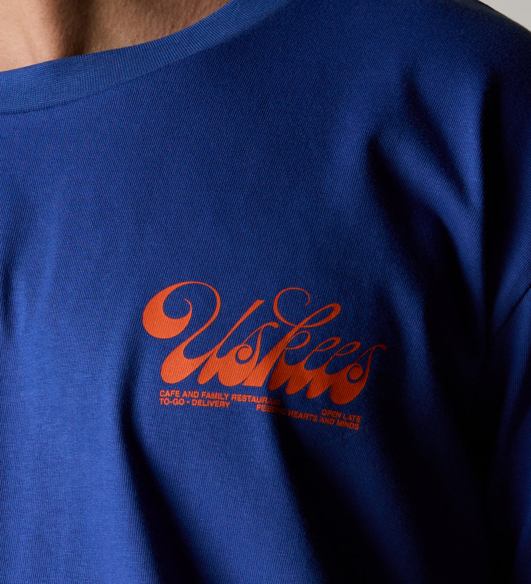 Wearing the uskees ultra blue men's 'diner' tee with a focus on the small bright orange 'diner' logo on the chest.