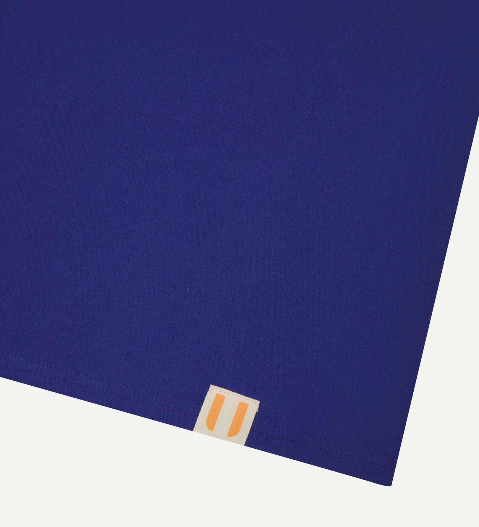 Hem close-up of Uskees ultra blue organic cotton T-shirt showing square branding label.