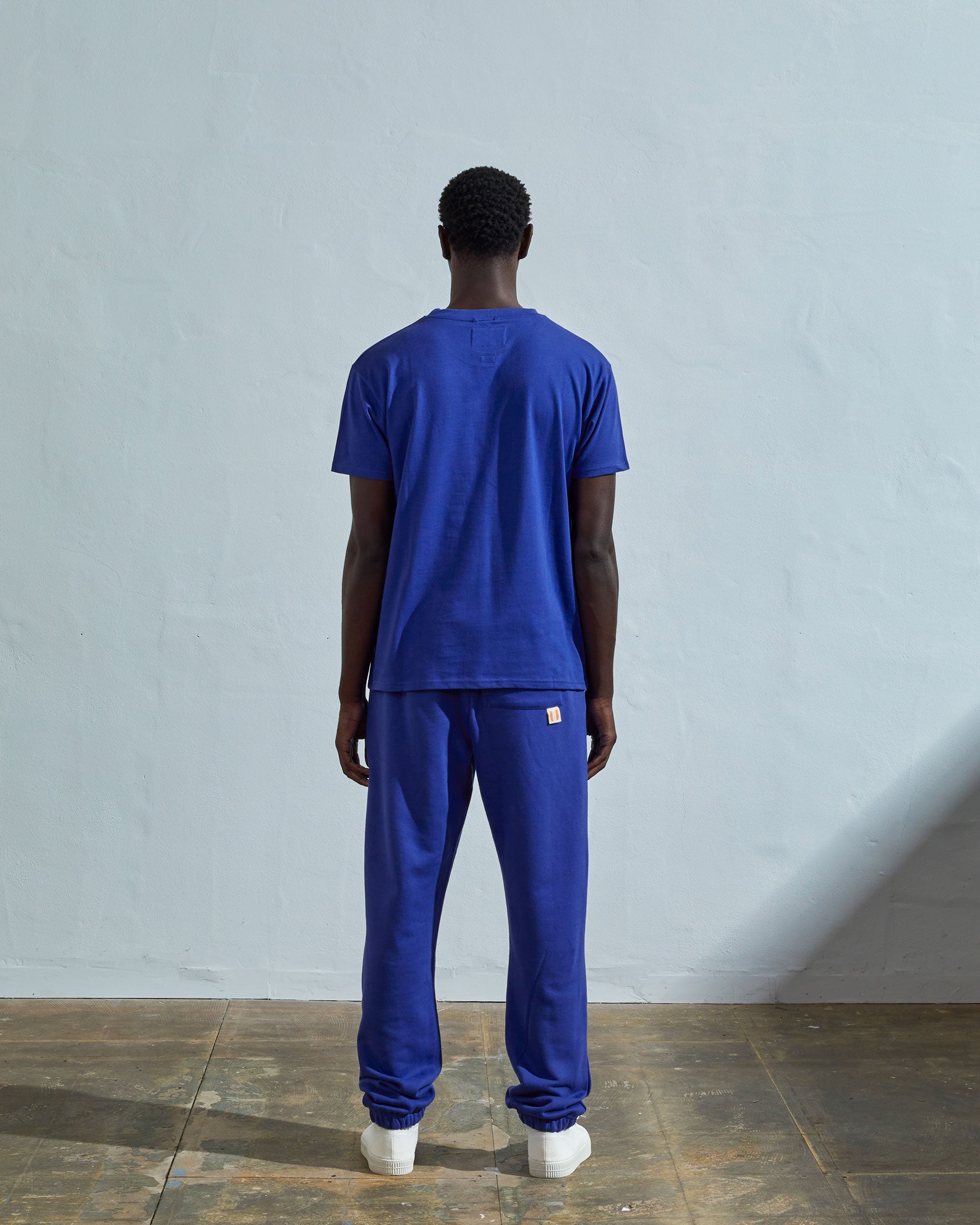 Full-length back view of model wearing ultra blue, relaxed cut organic cotton #7006 jersey T-shirt by Uskees paired with matching pants.