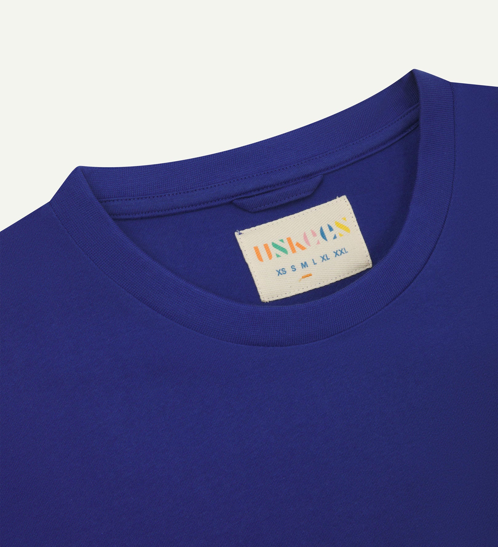 Neckline close-up of Uskees ultra blue organic cotton T-shirt showing hanging loop and branding label.