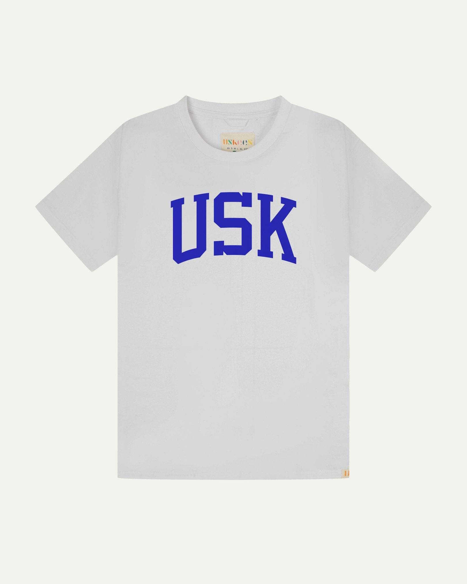 Full flat view of white organic cotton signature T-shirt for men, showing the varsity inspired 'USK' logo in blue on the chest, and the Uskees branding labels on the neck and hem.