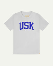 Full flat view of white organic cotton signature T-shirt for men, showing the varsity inspired 'USK' logo in blue on the chest, and the Uskees branding labels on the neck and hem.