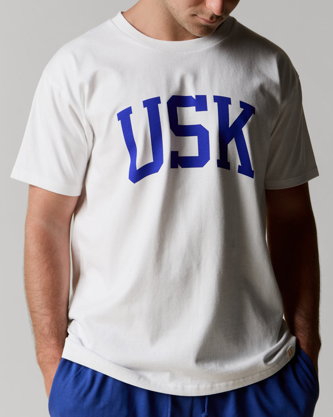 Model shot showing front of Uskees men's white short sleeve t-shirt with the signature USK logo on the front in blue.