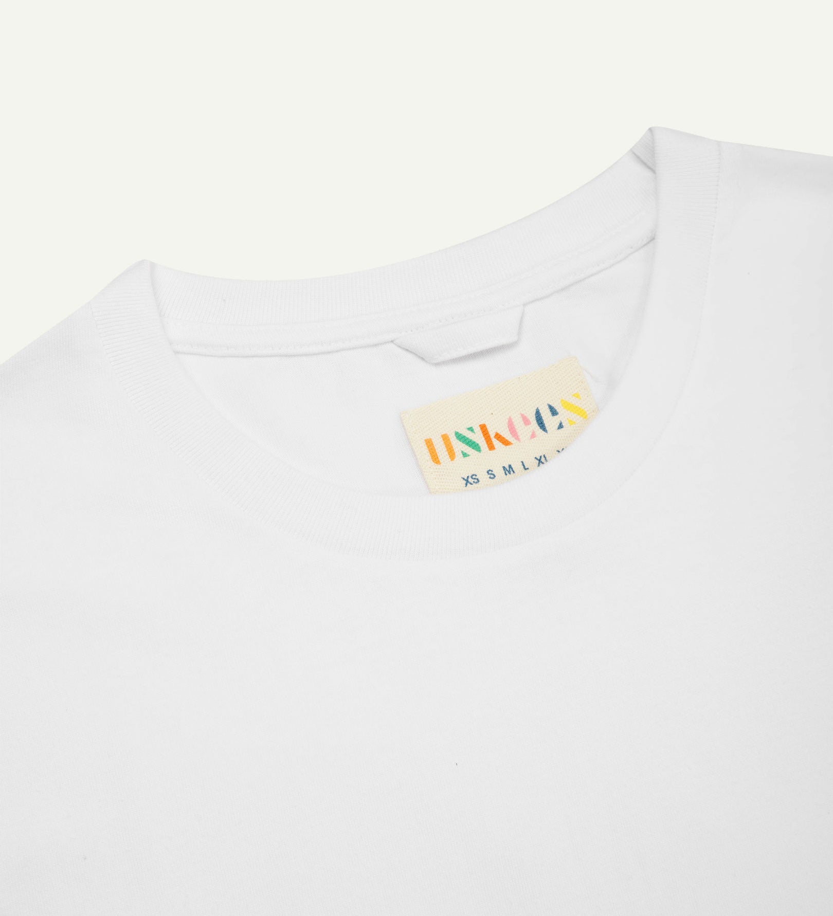 Neckline close-up of Uskees white organic cotton T-shirt showing hanging loop and branding label.