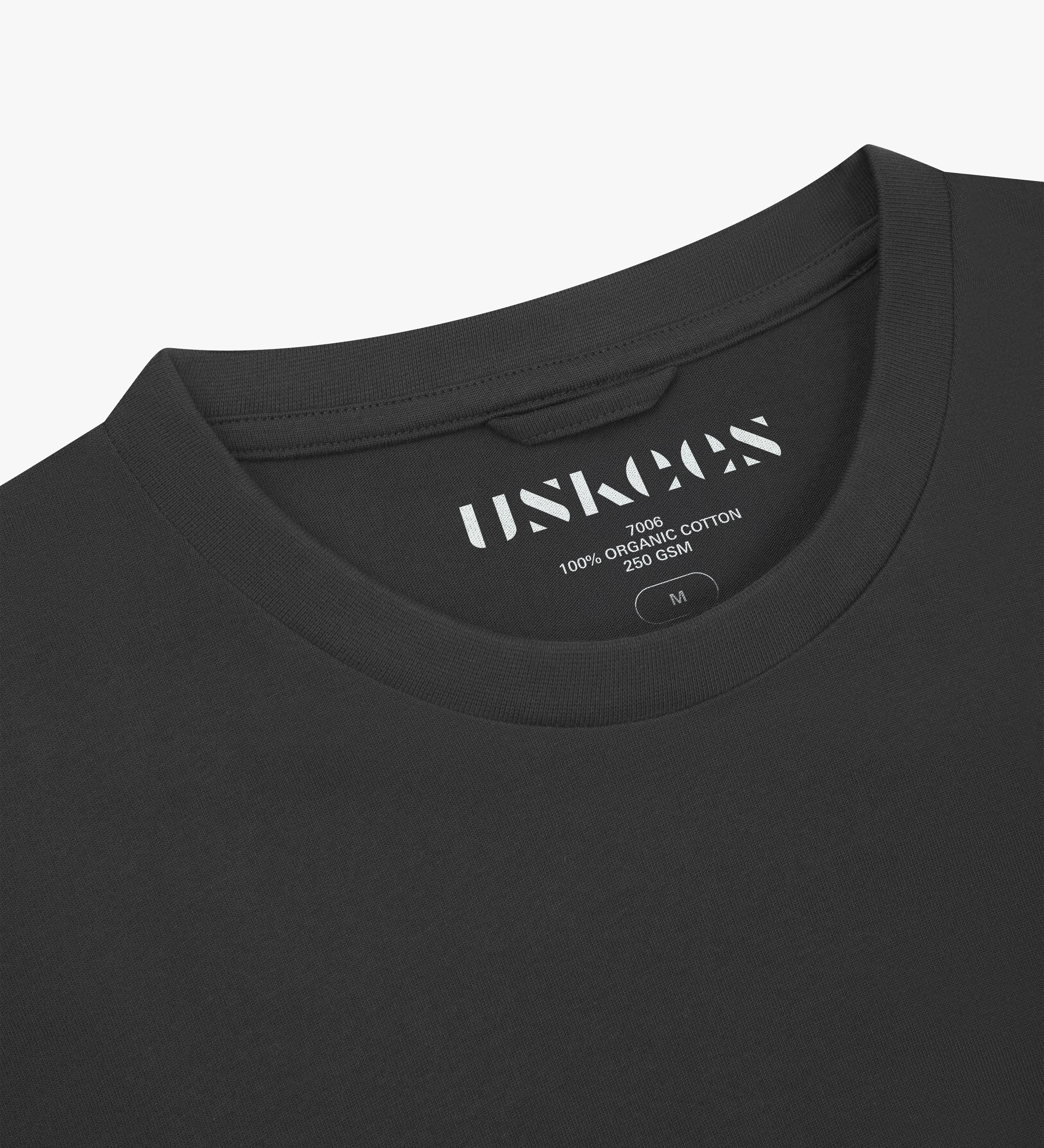Neckline close-up of Uskees faded black organic cotton T-shirt showing hanging loop and branding label.