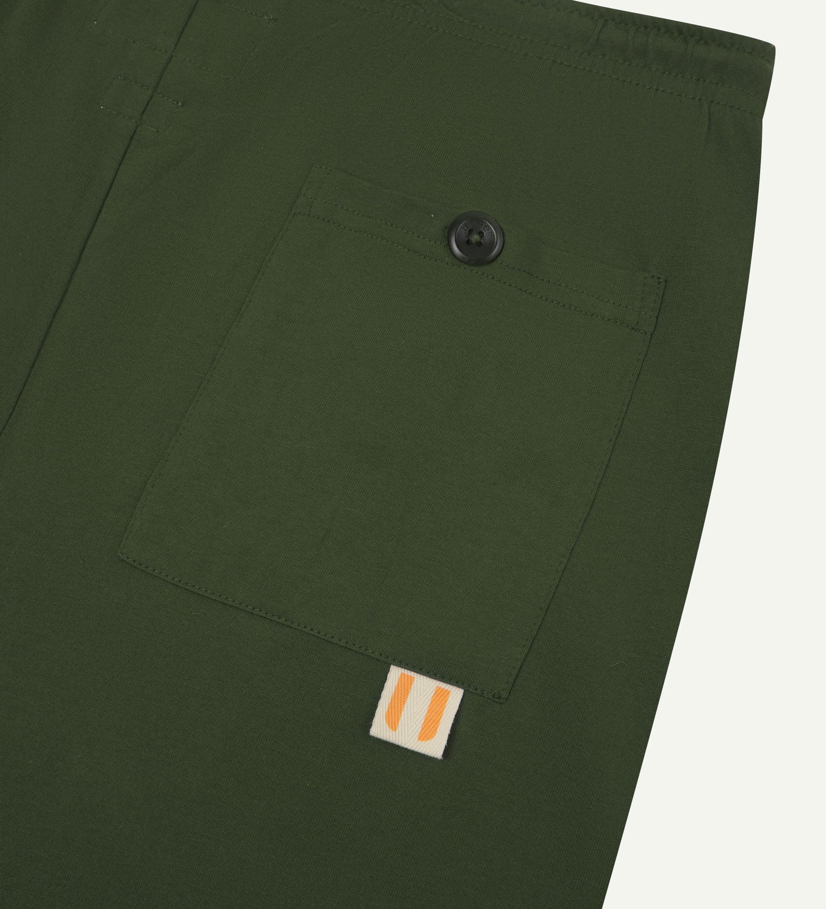 Close-up view of coriander-green organic cotton 7007 men's shorts against white background. Clear view of buttoned back pocket and Uskees logo label.