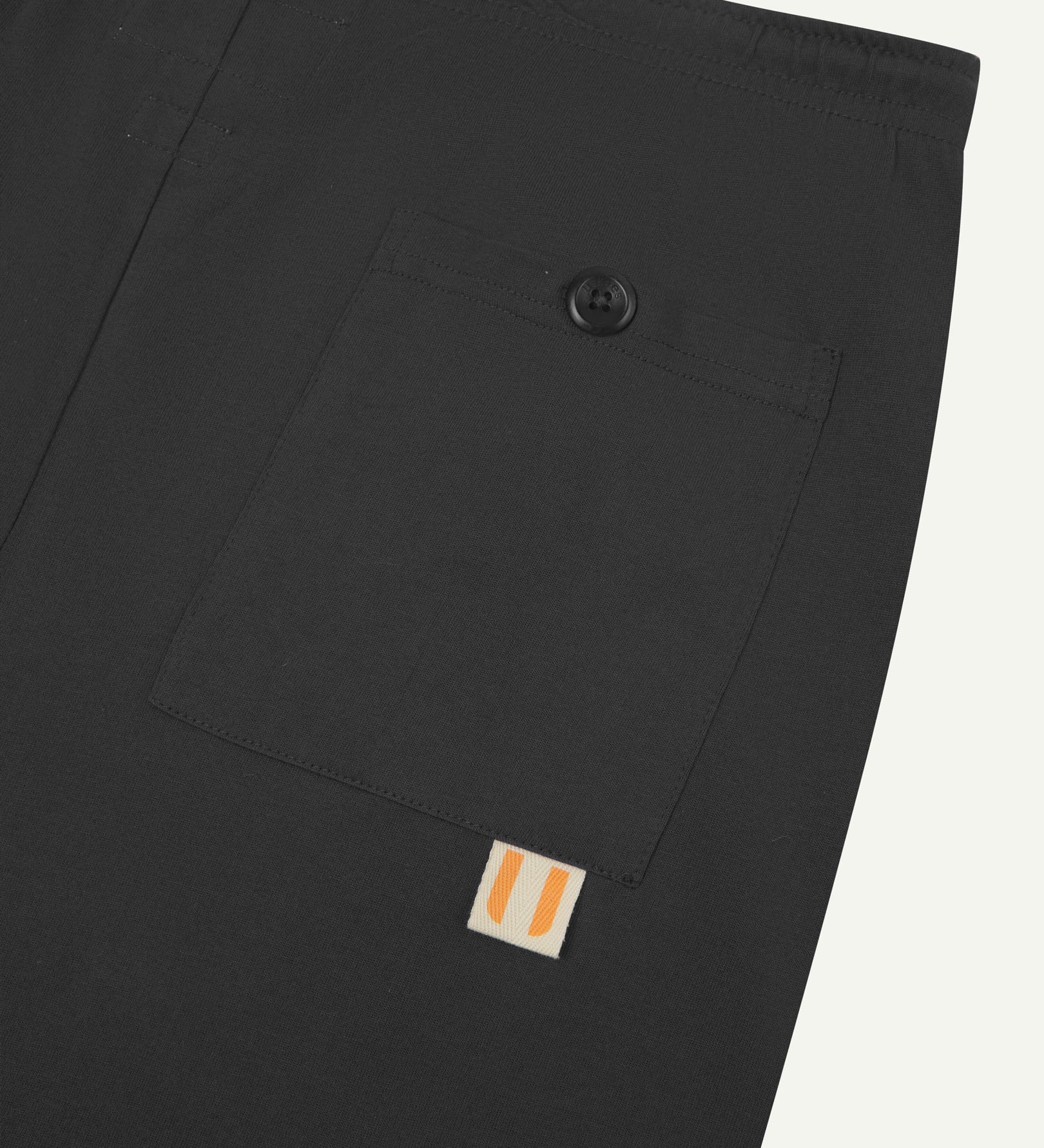 Close-up view of faded black organic cotton 7007 men's shorts against white background. Clear view of buttoned back pocket and Uskees logo label.