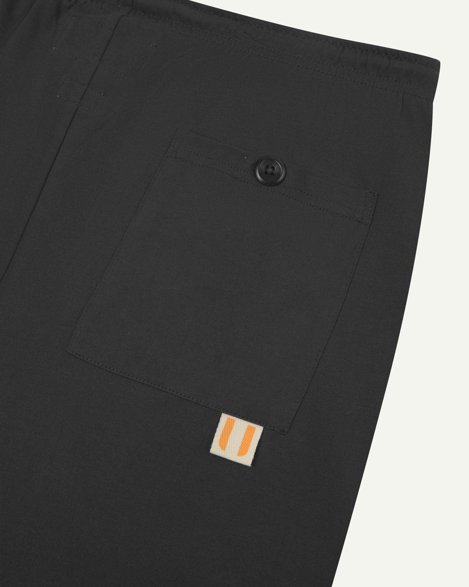 Close-up view of faded black organic cotton 7007 men's shorts against white background. Clear view of buttoned back pocket and Uskees logo label.