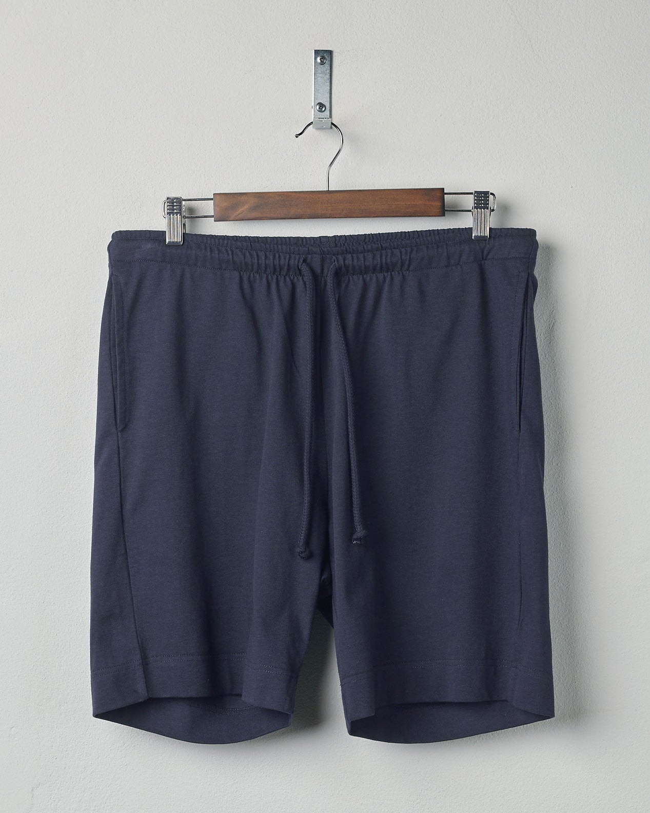 Front view of midnight blue organic cotton #7007 jersey shorts by Uskees, presented on hanger against white background. Clear view of drawstring waist and side pockets.
