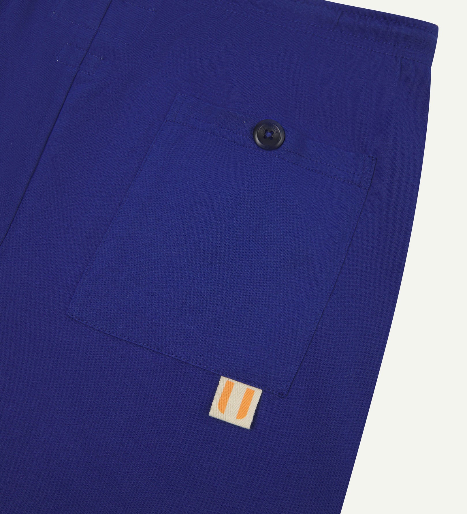 Close-up view of ultra blue organic cotton 7007 men's shorts against white background. Clear view of buttoned back pocket and Uskees logo label.