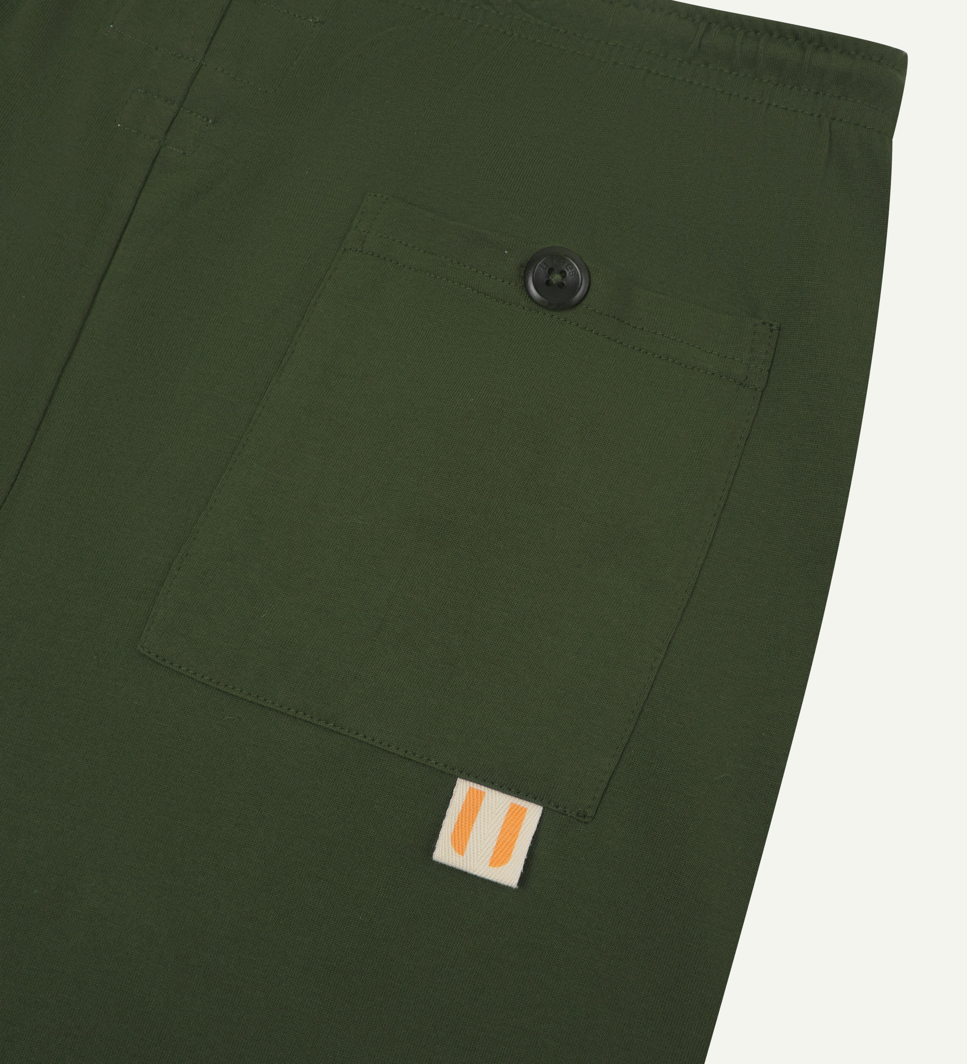 Close-up view of mid-green organic cotton #7007 jersey shorts against white background. Clear view of pocket and uskees logo label.