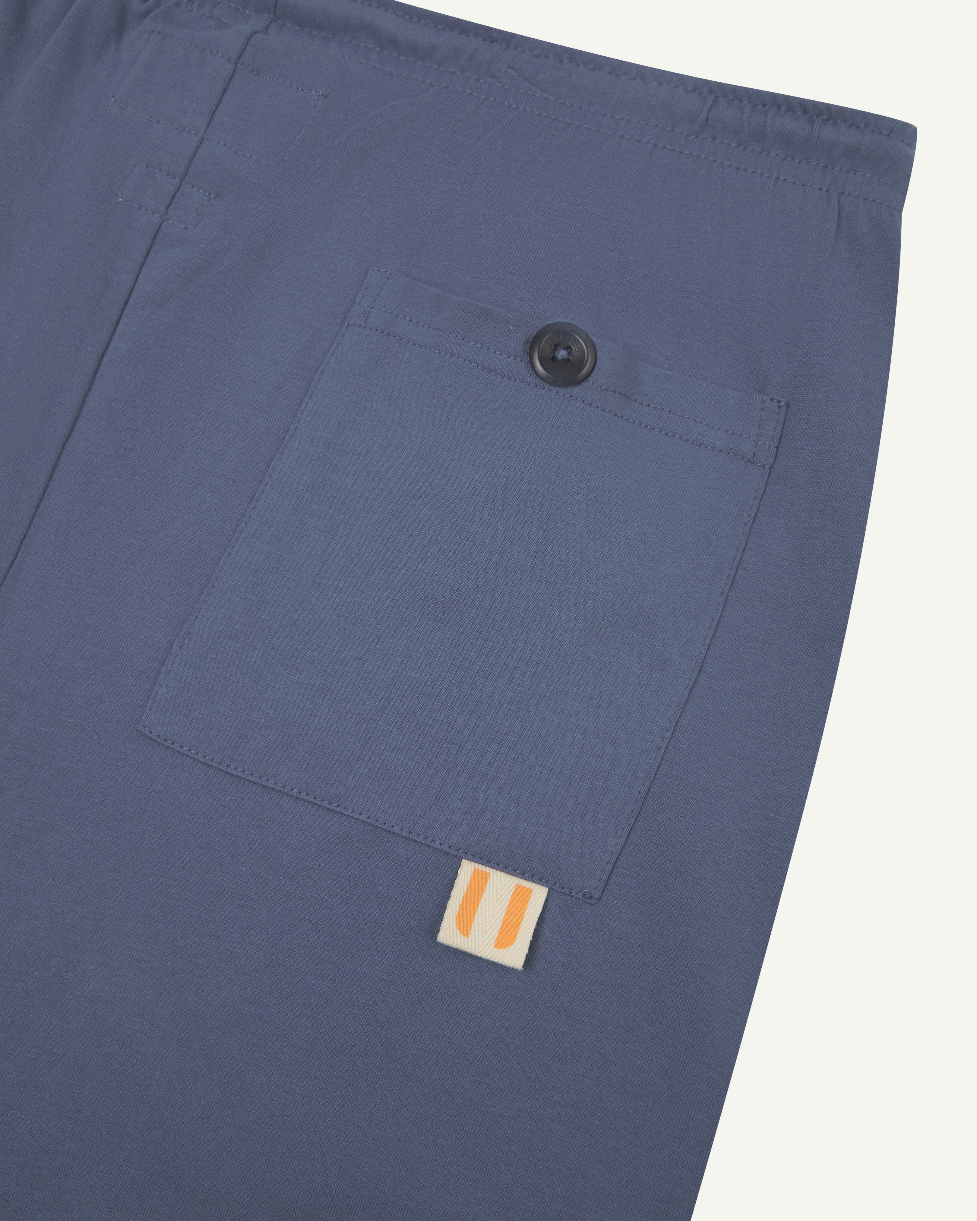 Close-up view of light blue organic cotton #7007 men's shorts against white background. Clear view of buttoned back pocket and uskees logo label.