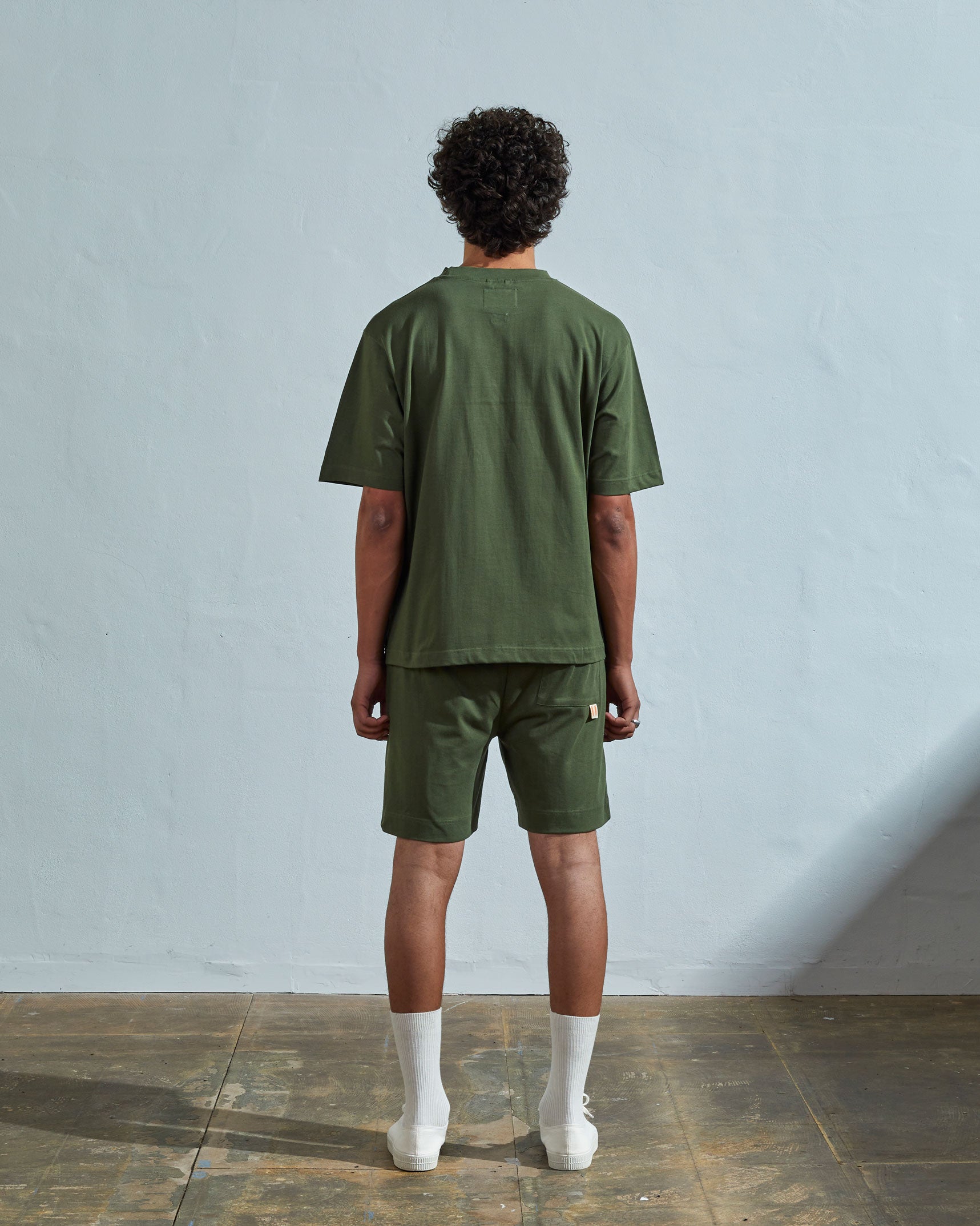Full-length back view of model wearing coriander-green, relaxed cut organic cotton #7008 oversized jersey T-shirt by Uskees paired with matching shorts.