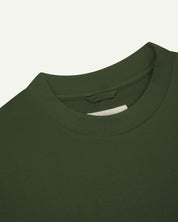 Neckline close-up of coriander-green organic cotton oversized T-shirt showing hanging loop and Uskees branding label.