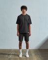 Full-length front view of model wearing faded black organic cotton #7008 oversized jersey T-shirt by Uskees paired with matching shorts.