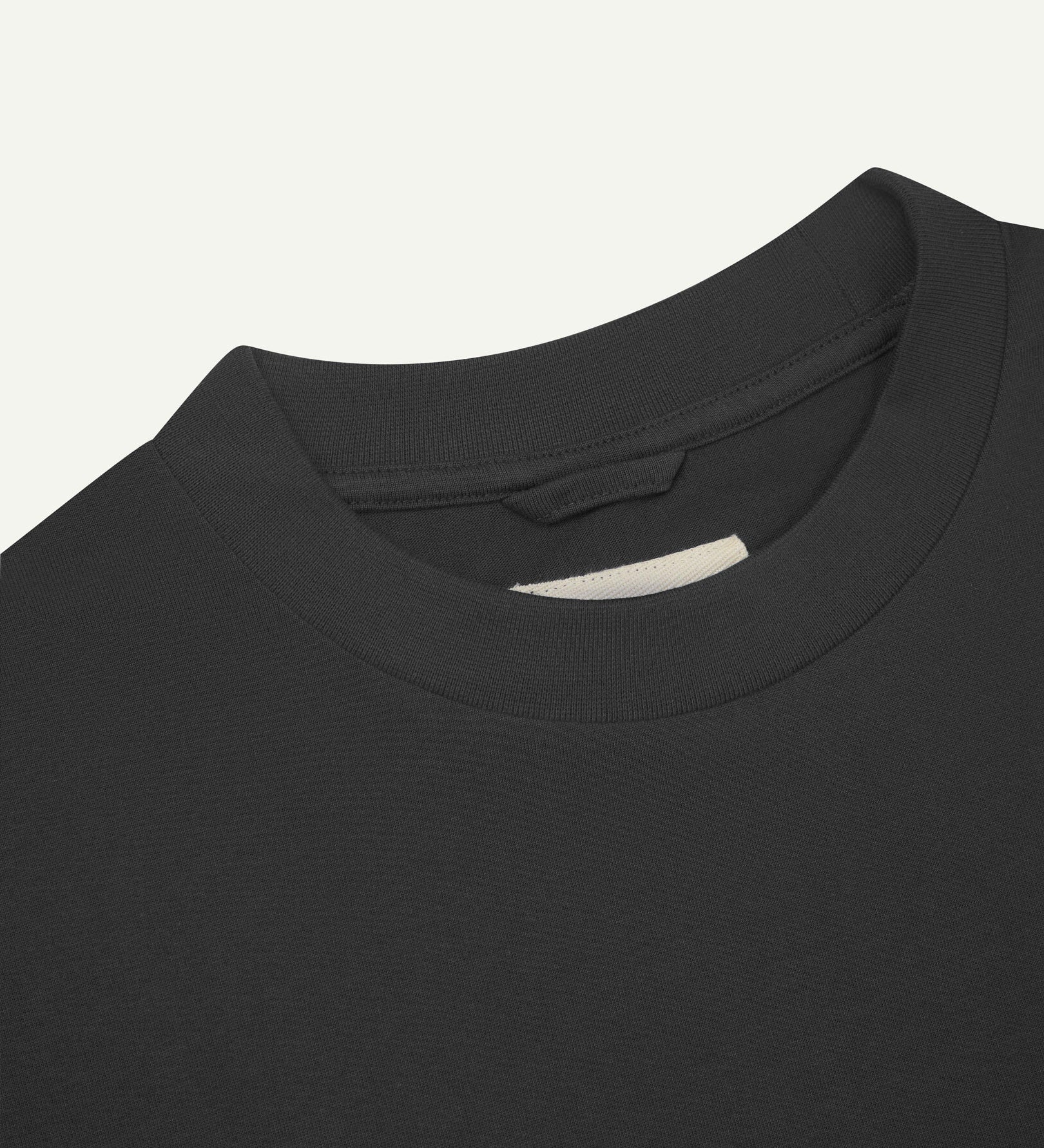 Neckline close-up of faded black organic cotton oversized T-shirt showing hanging loop and Uskees branding label.