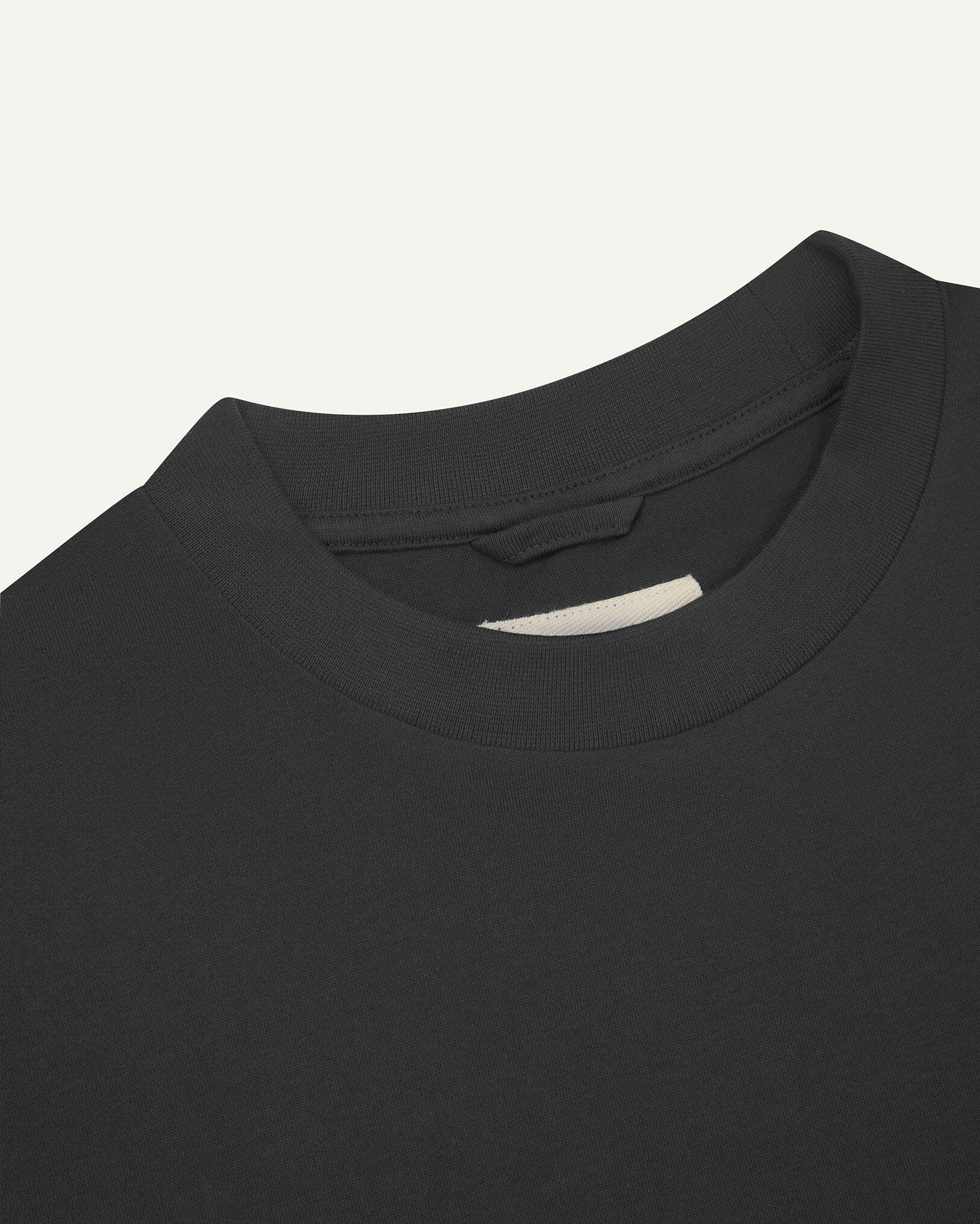 Neckline close-up of faded black organic cotton oversized T-shirt showing hanging loop and Uskees branding label.