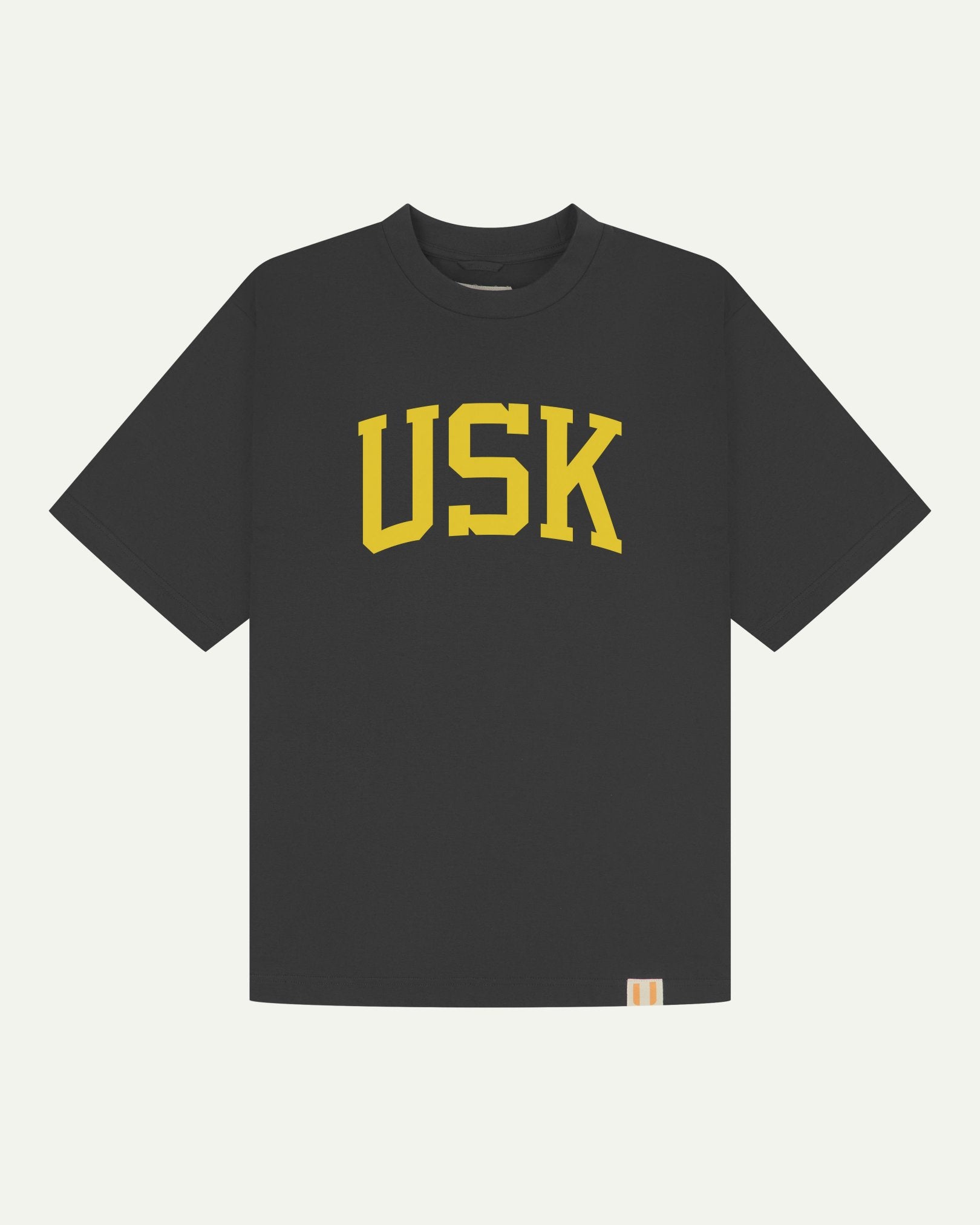 Full flat view of oversized faded black organic cotton signature T-shirt for men, showing the varsity inspired 'USK' logo in yellow on the chest, and the Uskees branding labels on the neck and hem.