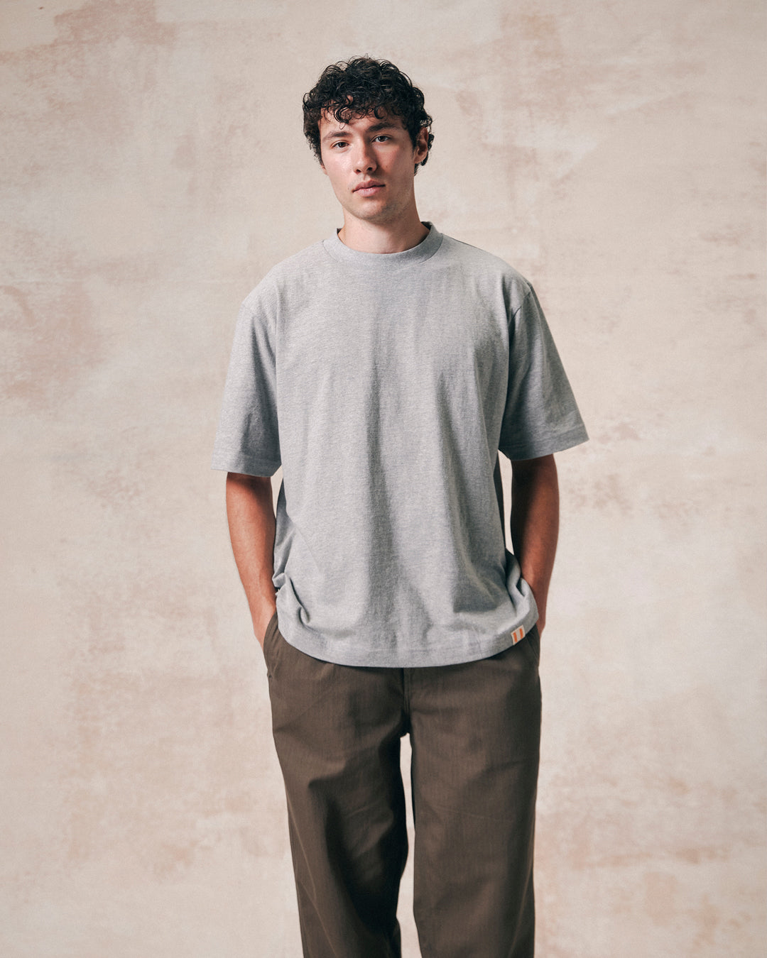 Front view of model wearing grey marl organic cotton #7008 oversized jersey T-shirt by Uskees paired with loose khaki pants.