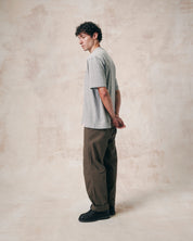 Side view of model wearing grey marl relaxed cut organic cotton #7008 oversized jersey T-shirt by Uskees paired with loose khaki pants.