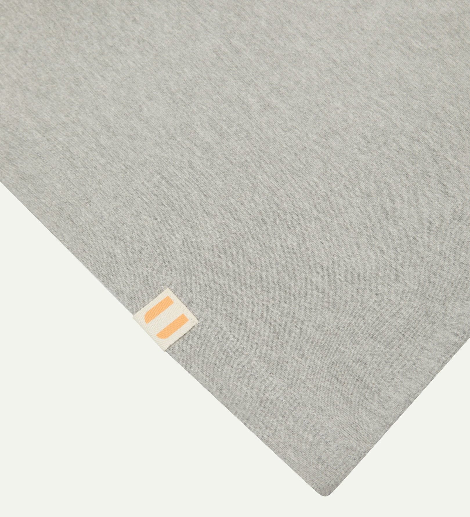 Hem close-up of the 7008 grey-marl organic cotton T-shirt showing texture of the medium weight organic cotton jersey and the small square Uskees branding tag.