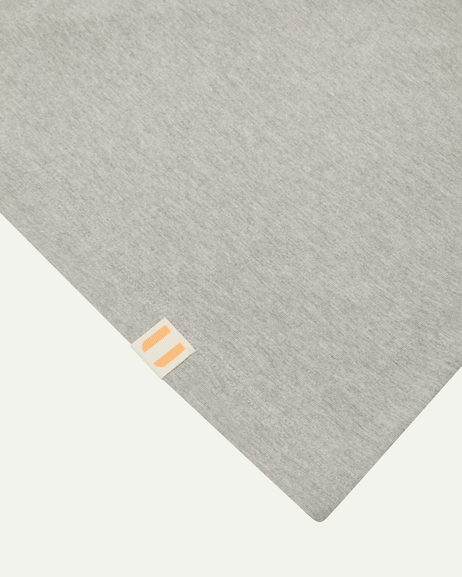 Hem close-up of the 7008 grey-marl organic cotton T-shirt showing texture of the medium weight organic cotton jersey and the small square Uskees branding tag.