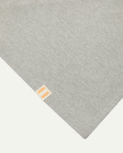 Hem close-up of the 7008 grey-marl organic cotton T-shirt showing texture of the medium weight organic cotton jersey and the small square Uskees branding tag.