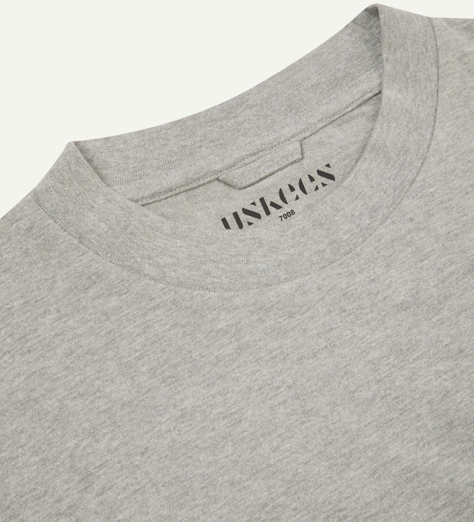 Neckline close-up of the oversized Uskees grey-marl organic cotton T-shirt showing hanging loop and branding stamp.