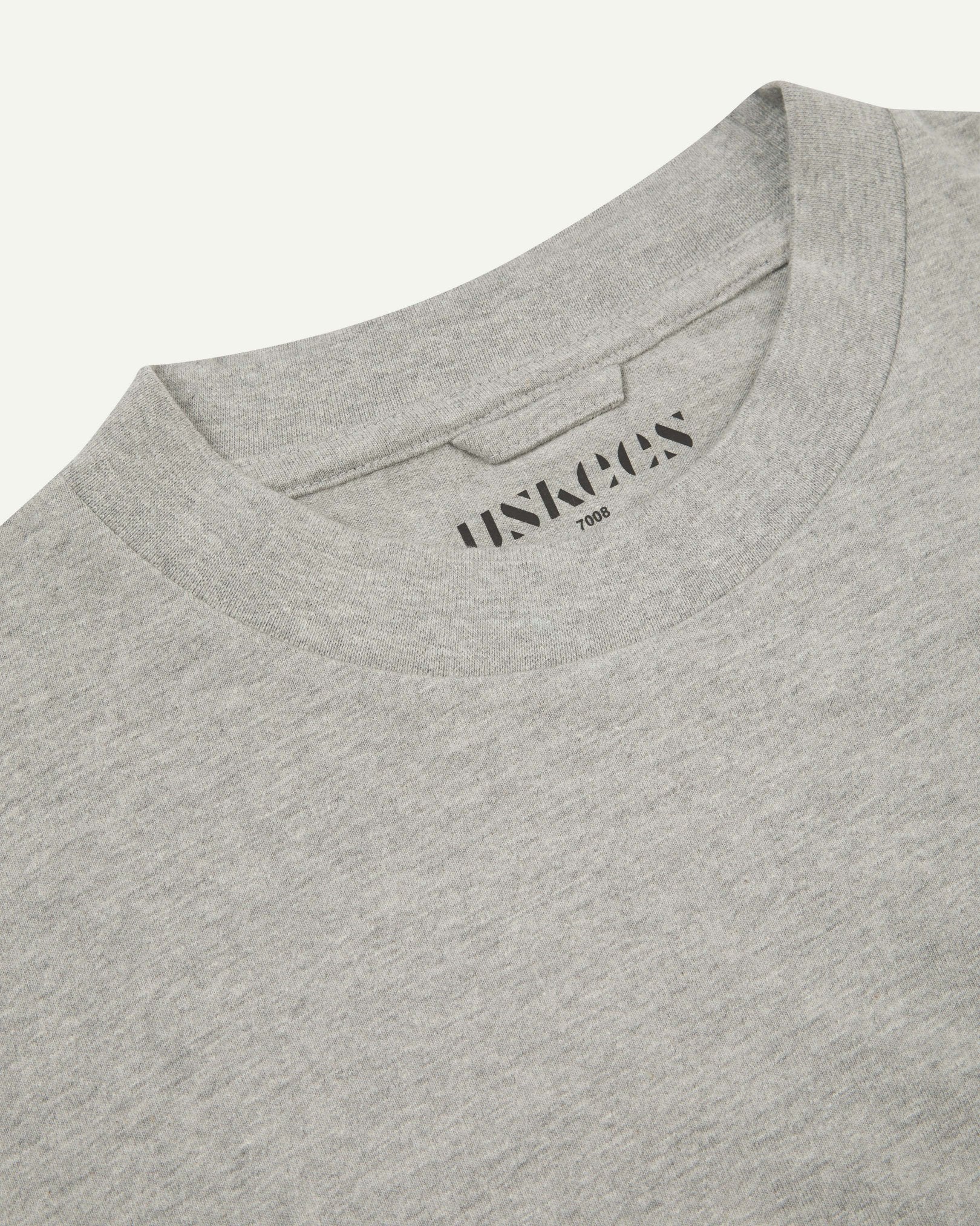 Neckline close-up of the oversized Uskees grey-marl organic cotton T-shirt showing hanging loop and branding stamp.